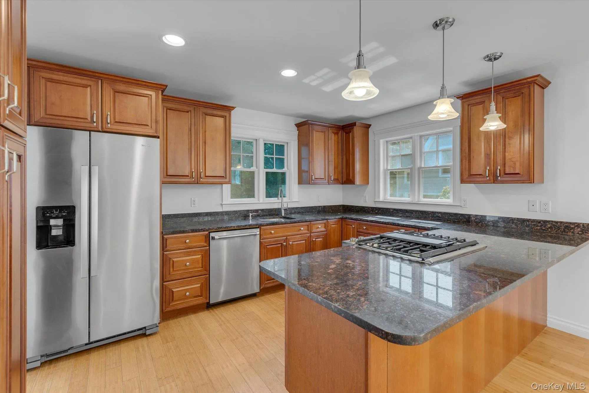Kitchen with brown cabinets, appliances with stainless steel finishes, a peninsula, dark stone countertops, and recessed lighting Kitchen with brown cabinets, appliances with stainless steel finishes, a peninsula, dark stone countertops, and recessed lighting