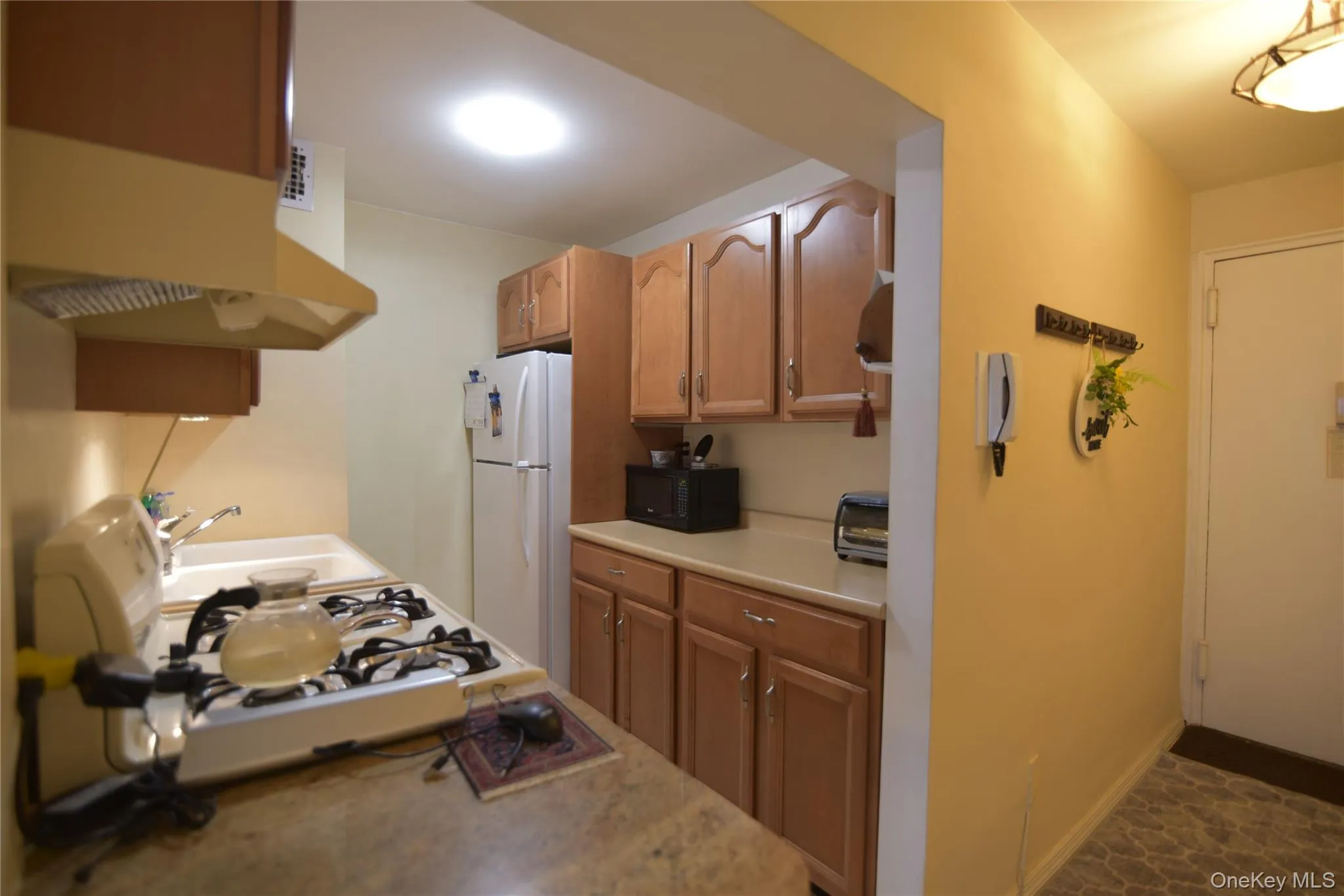 Kitchen with light countertops, white appliances, under cabinet range hood, and brown cabinets Kitchen with light countertops, white appliances, under cabinet range hood, and brown cabinets