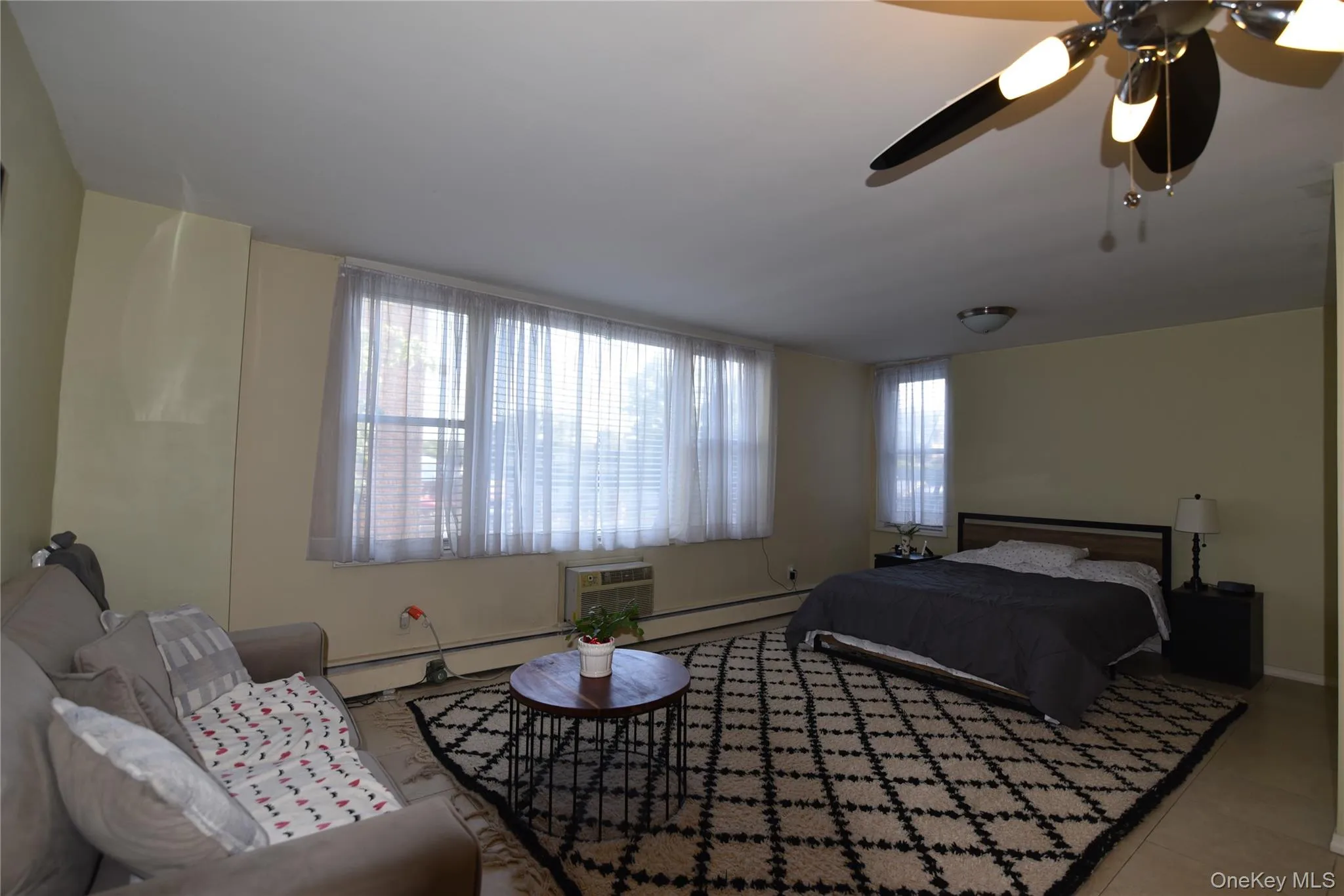 Bedroom featuring a ceiling fan, tile patterned flooring, a baseboard radiator, and a wall mounted AC Bedroom featuring a ceiling fan, tile patterned flooring, a baseboard radiator, and a wall mounted AC