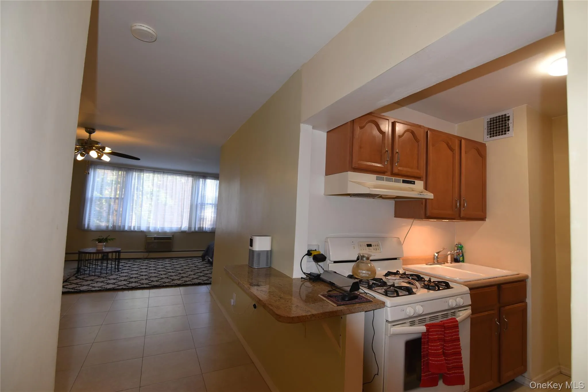 Kitchen featuring white range with gas stovetop, light tile patterned floors, brown cabinetry, and under cabinet range hood Kitchen featuring white range with gas stovetop, light tile patterned floors, brown cabinetry, and under cabinet range hood