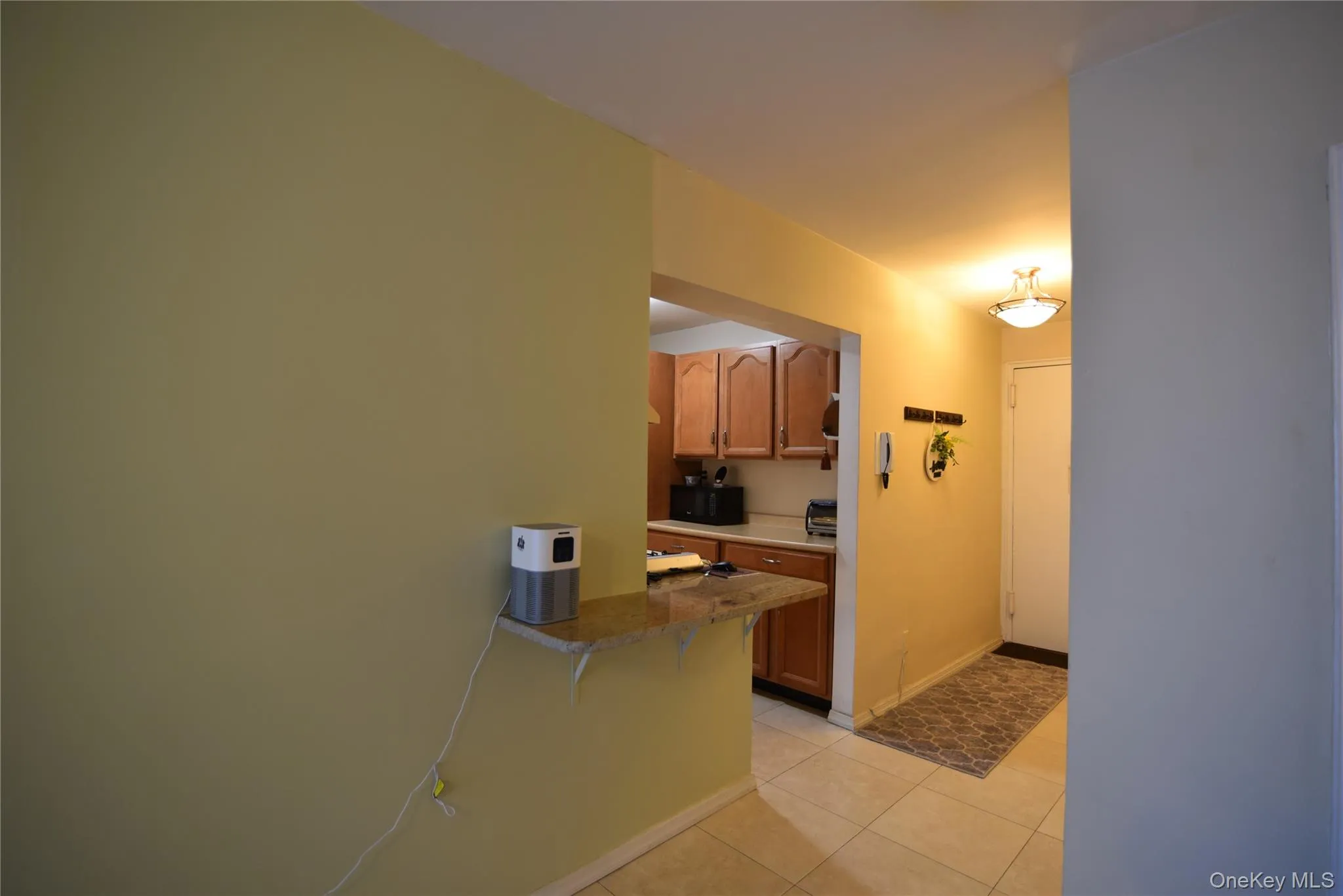 Kitchen with a kitchen breakfast bar, brown cabinets, light tile patterned floors, black microwave, and dark stone counters Kitchen with a kitchen breakfast bar, brown cabinets, light tile patterned floors, black microwave, and dark stone counters