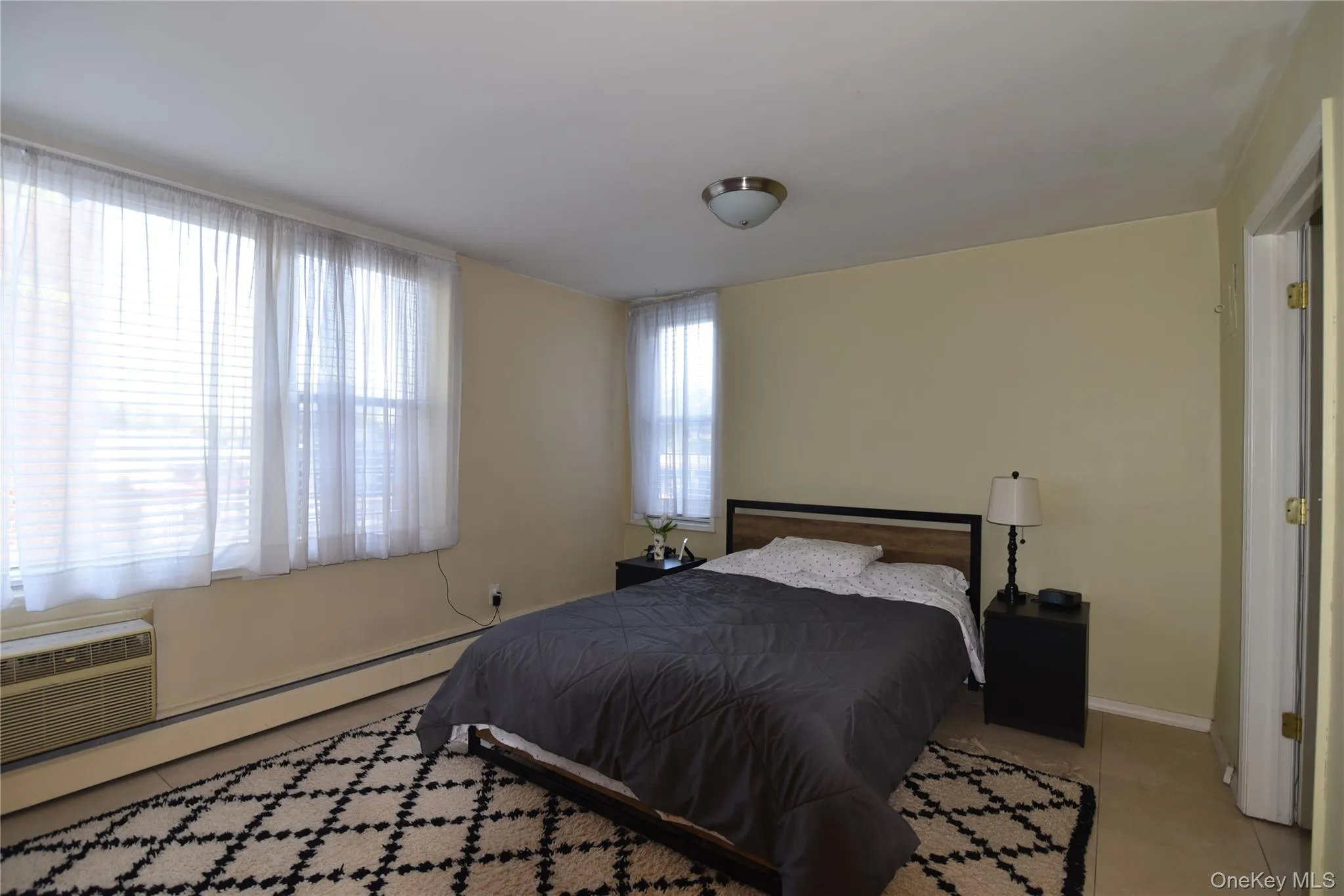 Tiled bedroom with a baseboard heating unit and a wall mounted air conditioner Tiled bedroom with a baseboard heating unit and a wall mounted air conditioner