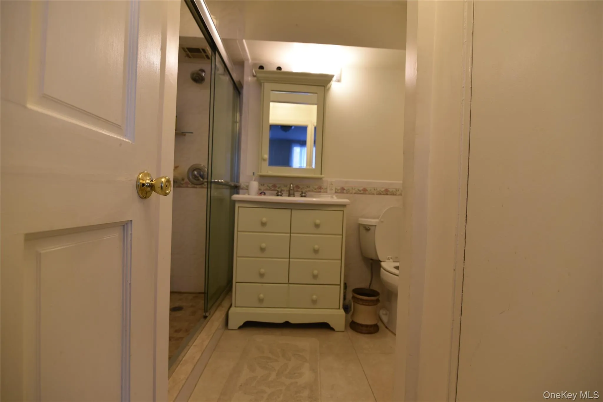 Full bath with vanity, a shower stall, light tile patterned floors, a wainscoted wall, and tile walls Full bath with vanity, a shower stall, light tile patterned floors, a wainscoted wall, and tile walls