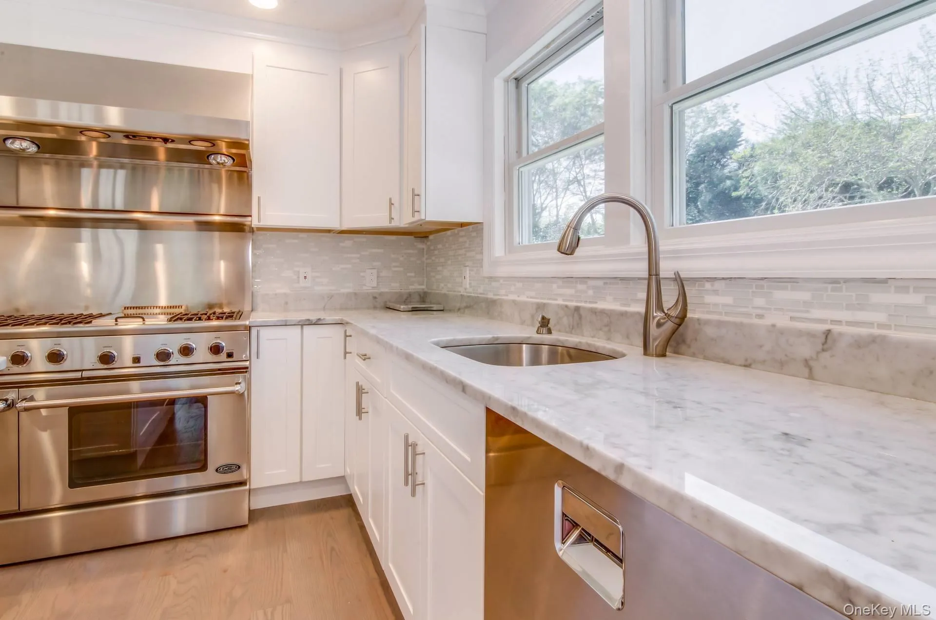 Kitchen featuring stainless steel appliances, light stone countertops, white cabinets, backsplash, and light wood finished floors Kitchen featuring stainless steel appliances, light stone countertops, white cabinets, backsplash, and light wood finished floors
