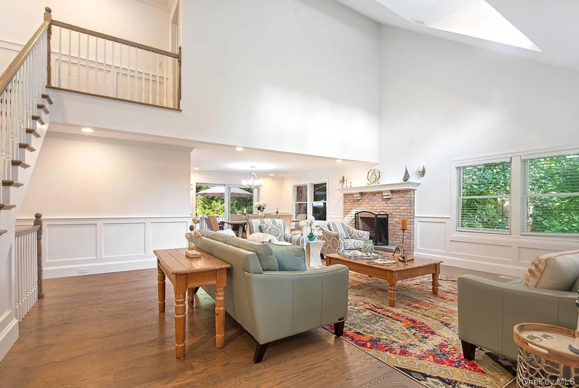 Living room featuring a decorative wall, a high ceiling, wood finished floors, a brick fireplace, and a wainscoted wall Living room featuring a decorative wall, a high ceiling, wood finished floors, a brick fireplace, and a wainscoted wall