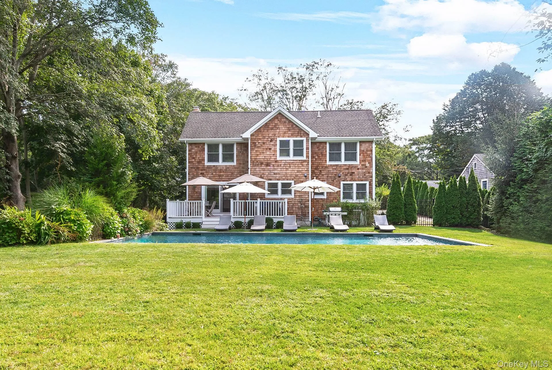 Back of property with an outdoor pool, a chimney, a yard, roof with shingles, and a wooden deck Back of property with an outdoor pool, a chimney, a yard, roof with shingles, and a wooden deck