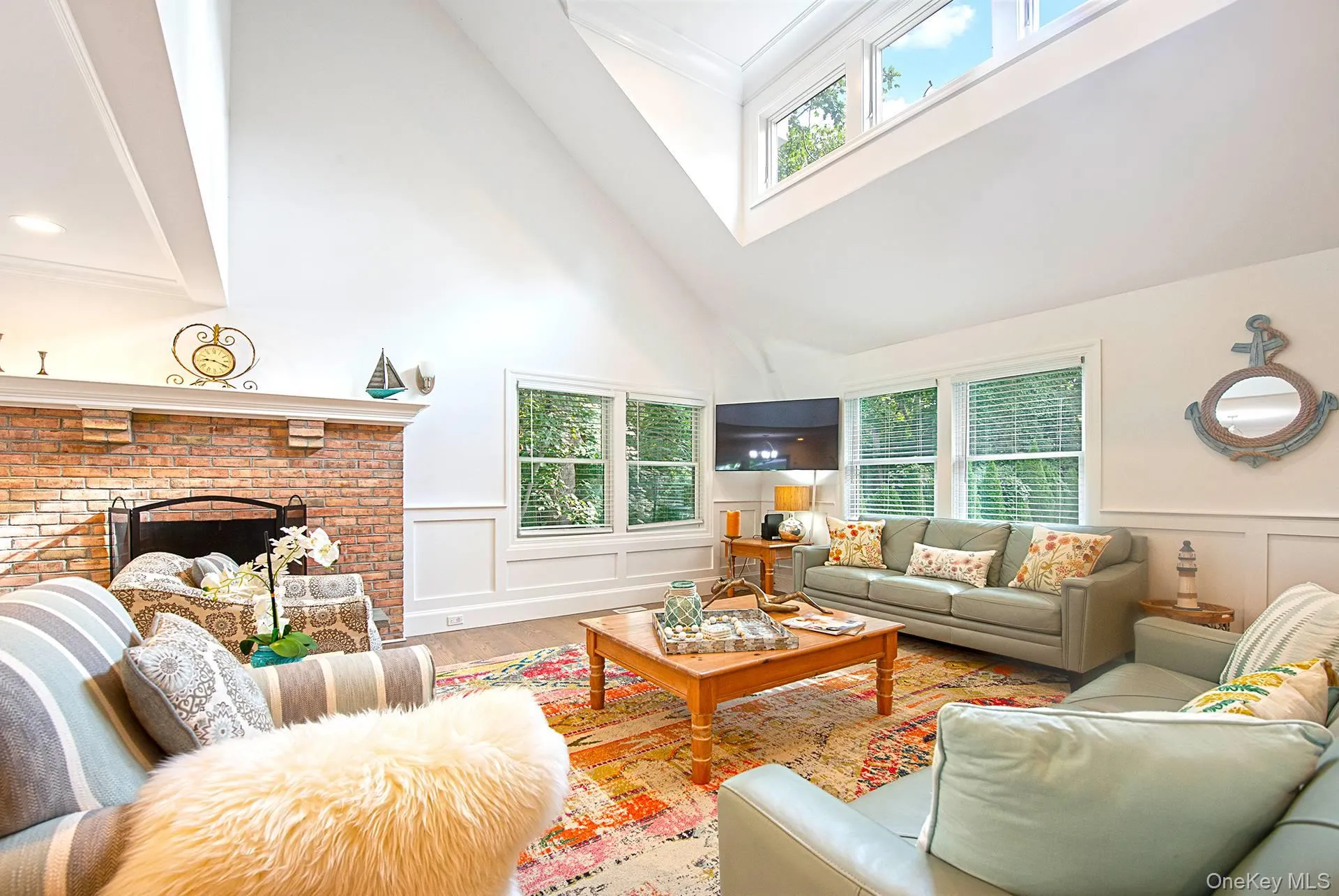 Living room featuring a decorative wall, a brick fireplace, wainscoting, healthy amount of natural light, and crown molding Living room featuring a decorative wall, a brick fireplace, wainscoting, healthy amount of natural light, and crown molding
