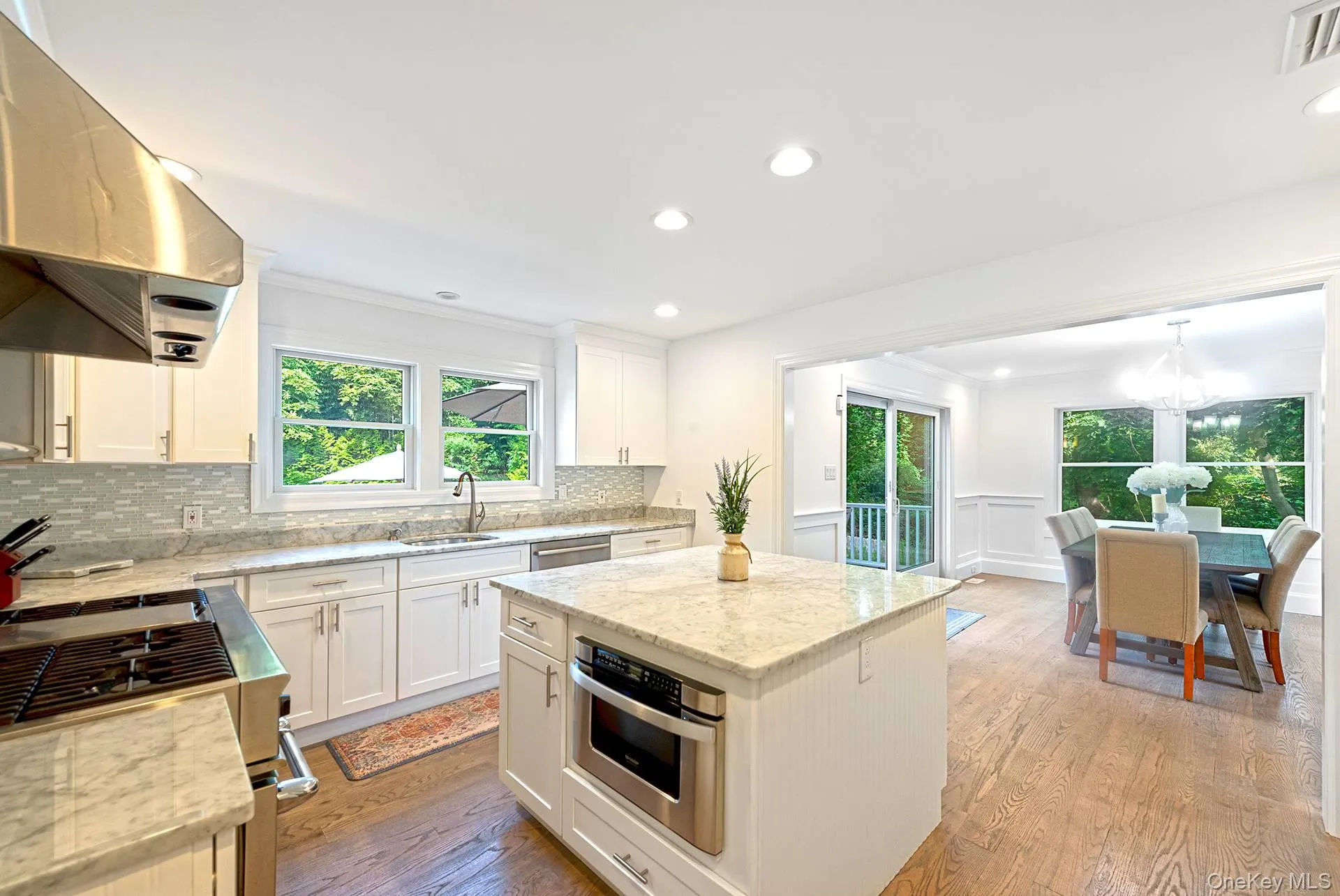 Kitchen with stainless steel appliances, extractor fan, white cabinets, light wood-style floors, and a center island Kitchen with stainless steel appliances, extractor fan, white cabinets, light wood-style floors, and a center island