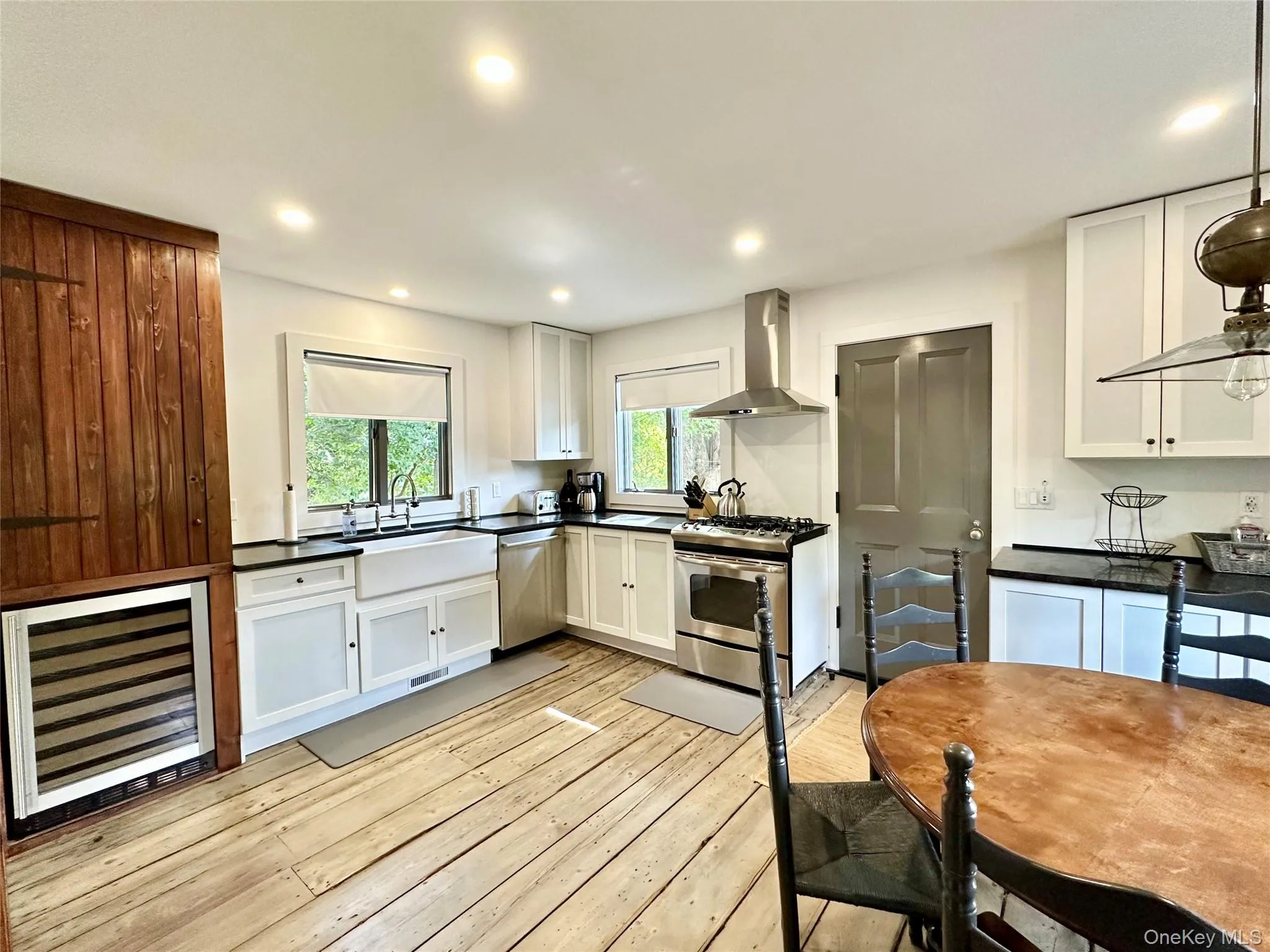 Kitchen with beverage cooler, wall chimney exhaust hood, appliances with stainless steel finishes, pendant lighting, and white cabinetry Kitchen with beverage cooler, wall chimney exhaust hood, appliances with stainless steel finishes, pendant lighting, and white cabinetry