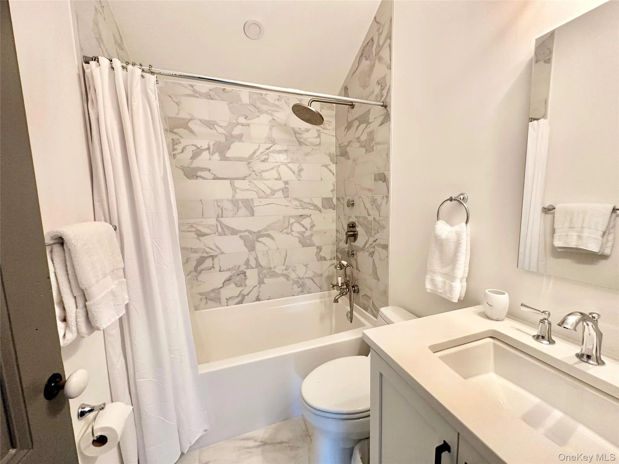 Bathroom featuring shower / bath combo, vanity, and light marble finish flooring Bathroom featuring shower / bath combo, vanity, and light marble finish flooring