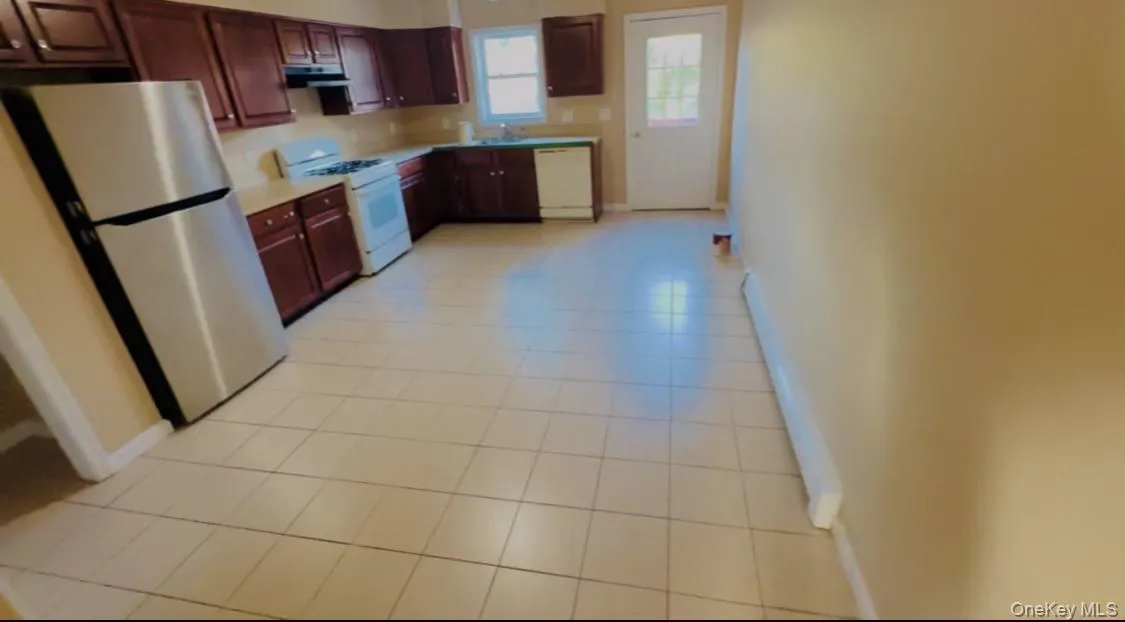 Kitchen with white appliances, light countertops, light tile patterned floors, and under cabinet range hood Kitchen with white appliances, light countertops, light tile patterned floors, and under cabinet range hood