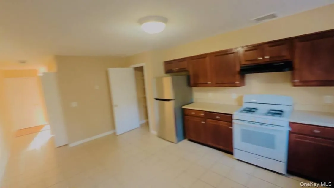 Kitchen with white range oven, light countertops, freestanding refrigerator, and under cabinet range hood Kitchen with white range oven, light countertops, freestanding refrigerator, and under cabinet range hood