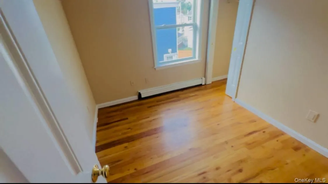 Empty room with light wood-style flooring and a baseboard heating unit Empty room with light wood-style flooring and a baseboard heating unit