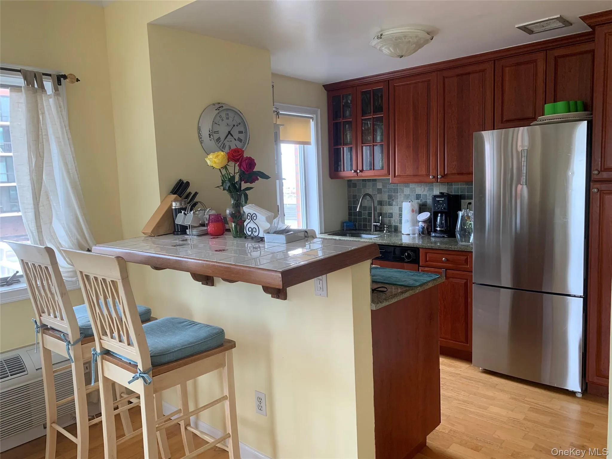 Kitchen featuring light wood finished floors, freestanding refrigerator, a breakfast bar area, a peninsula, and backsplash Kitchen featuring light wood finished floors, freestanding refrigerator, a breakfast bar area, a peninsula, and backsplash