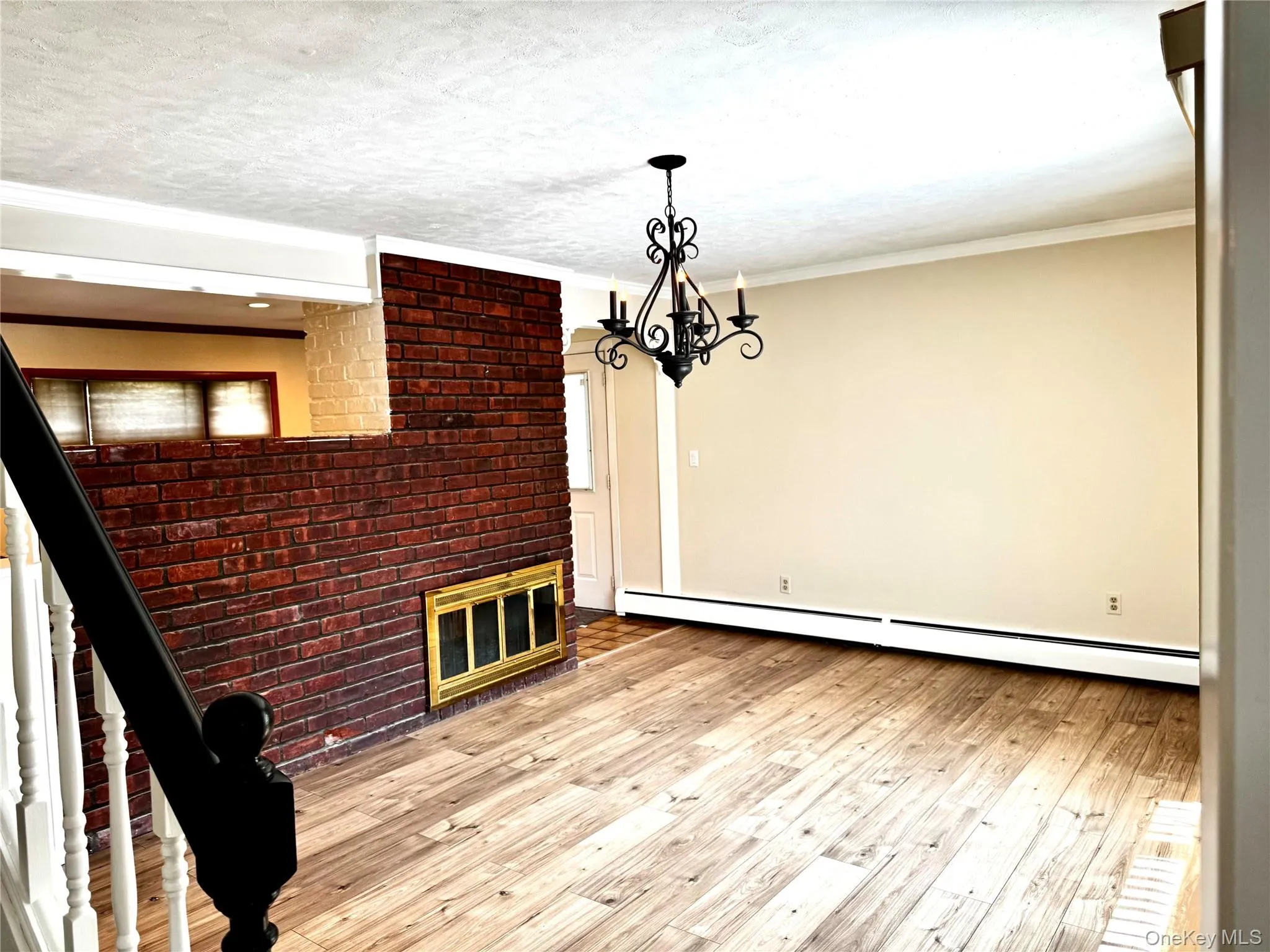 Unfurnished dining area featuring light wood-style floors, a baseboard radiator, a chandelier, a brick fireplace, and ornamental molding Unfurnished dining area featuring light wood-style floors, a baseboard radiator, a chandelier, a brick fireplace, and ornamental molding