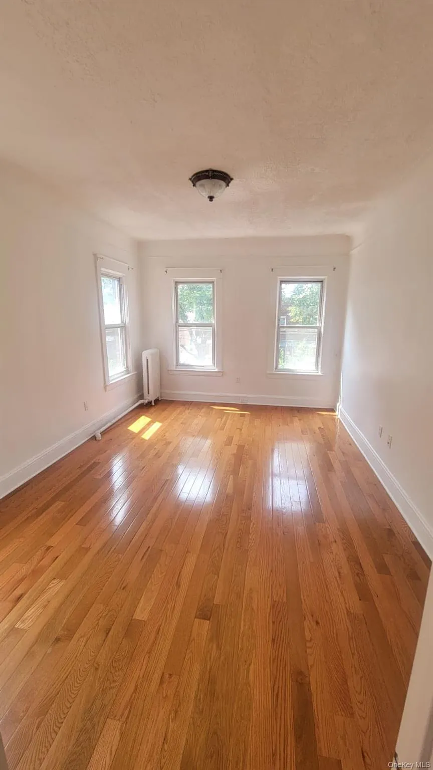 Unfurnished room with light wood finished floors, radiator, and a textured ceiling Unfurnished room with light wood finished floors, radiator, and a textured ceiling