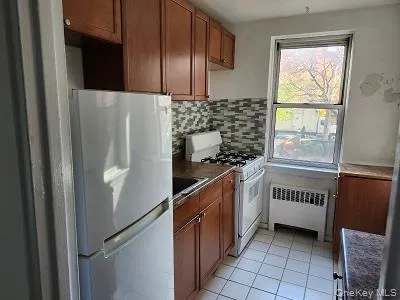 Kitchen featuring white appliances, dark countertops, light tile patterned floors, radiator heating unit, and decorative backsplash Kitchen featuring white appliances, dark countertops, light tile patterned floors, radiator heating unit, and decorative backsplash