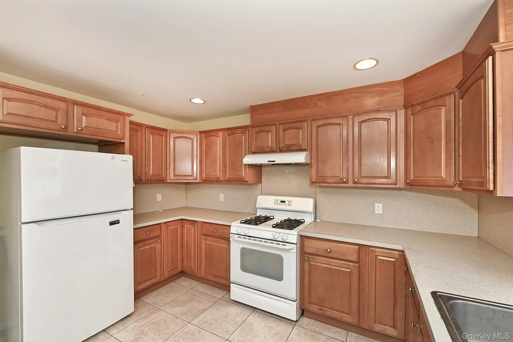 Kitchen featuring white appliances, light tile patterned floors, light countertops, brown cabinetry, and recessed lighting Kitchen featuring white appliances, light tile patterned floors, light countertops, brown cabinetry, and recessed lighting