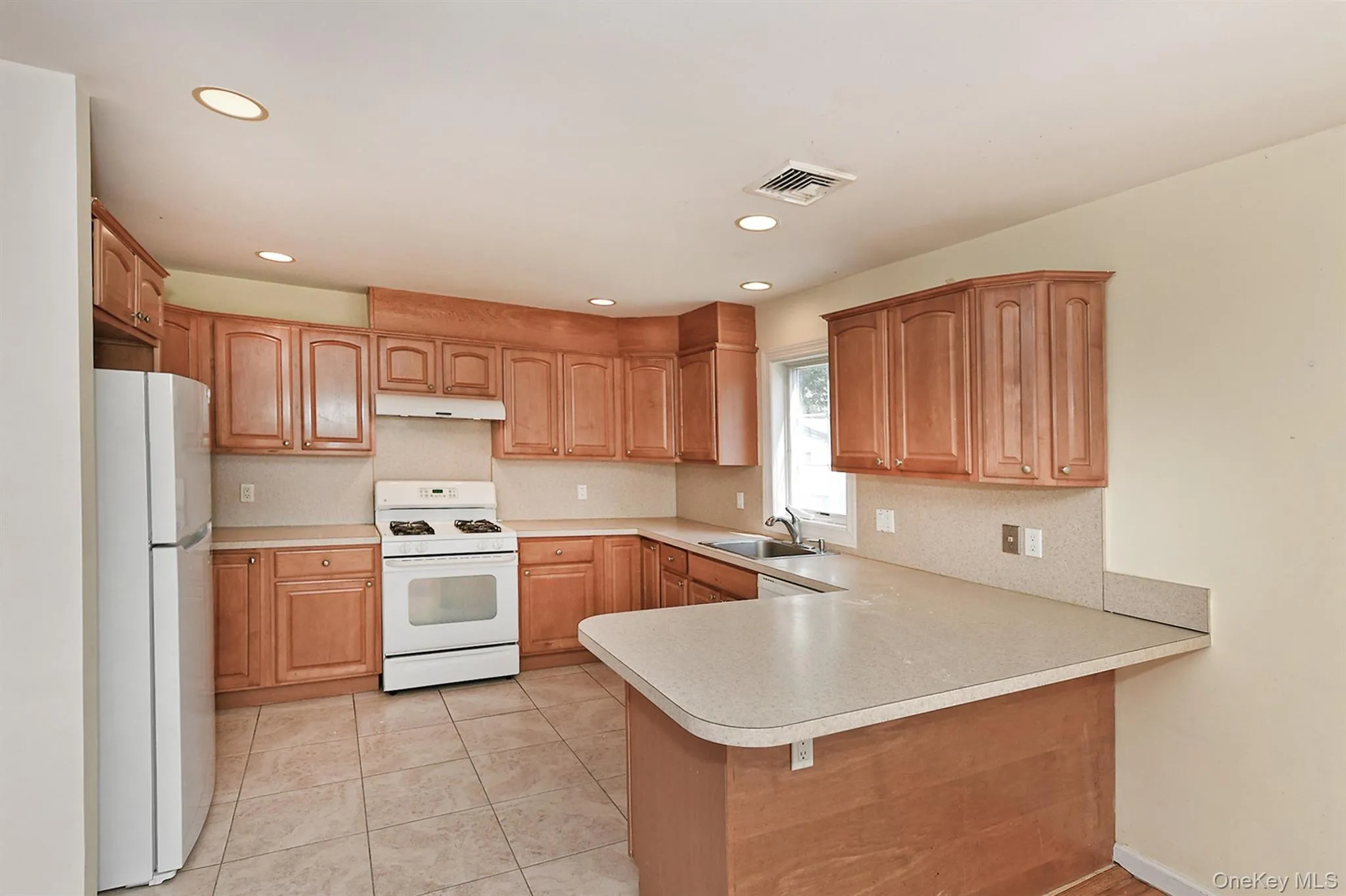 Kitchen featuring white appliances, a peninsula, light countertops, light tile patterned flooring, and recessed lighting Kitchen featuring white appliances, a peninsula, light countertops, light tile patterned flooring, and recessed lighting