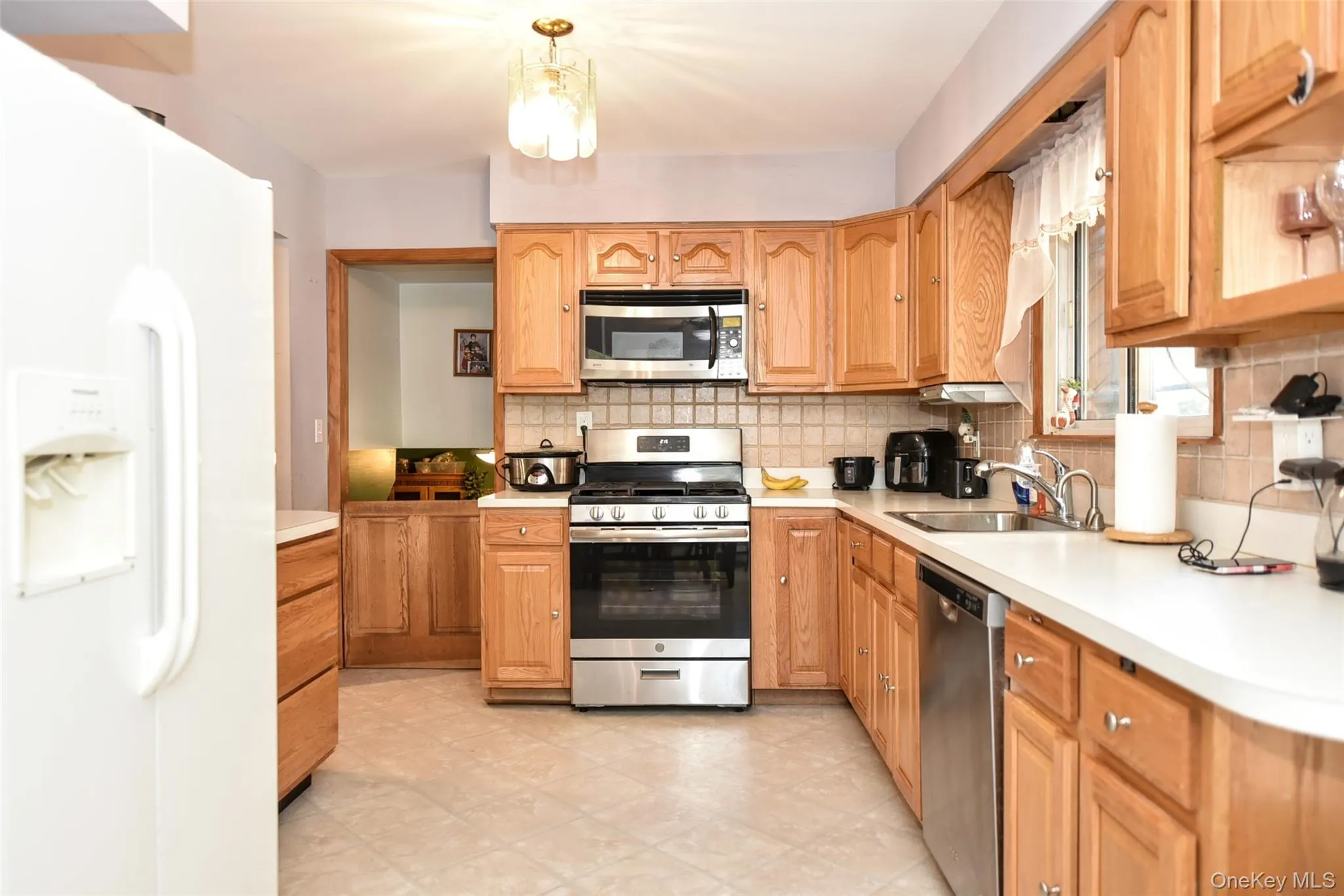 Kitchen featuring stainless steel appliances, decorative backsplash, and light countertops Kitchen featuring stainless steel appliances, decorative backsplash, and light countertops