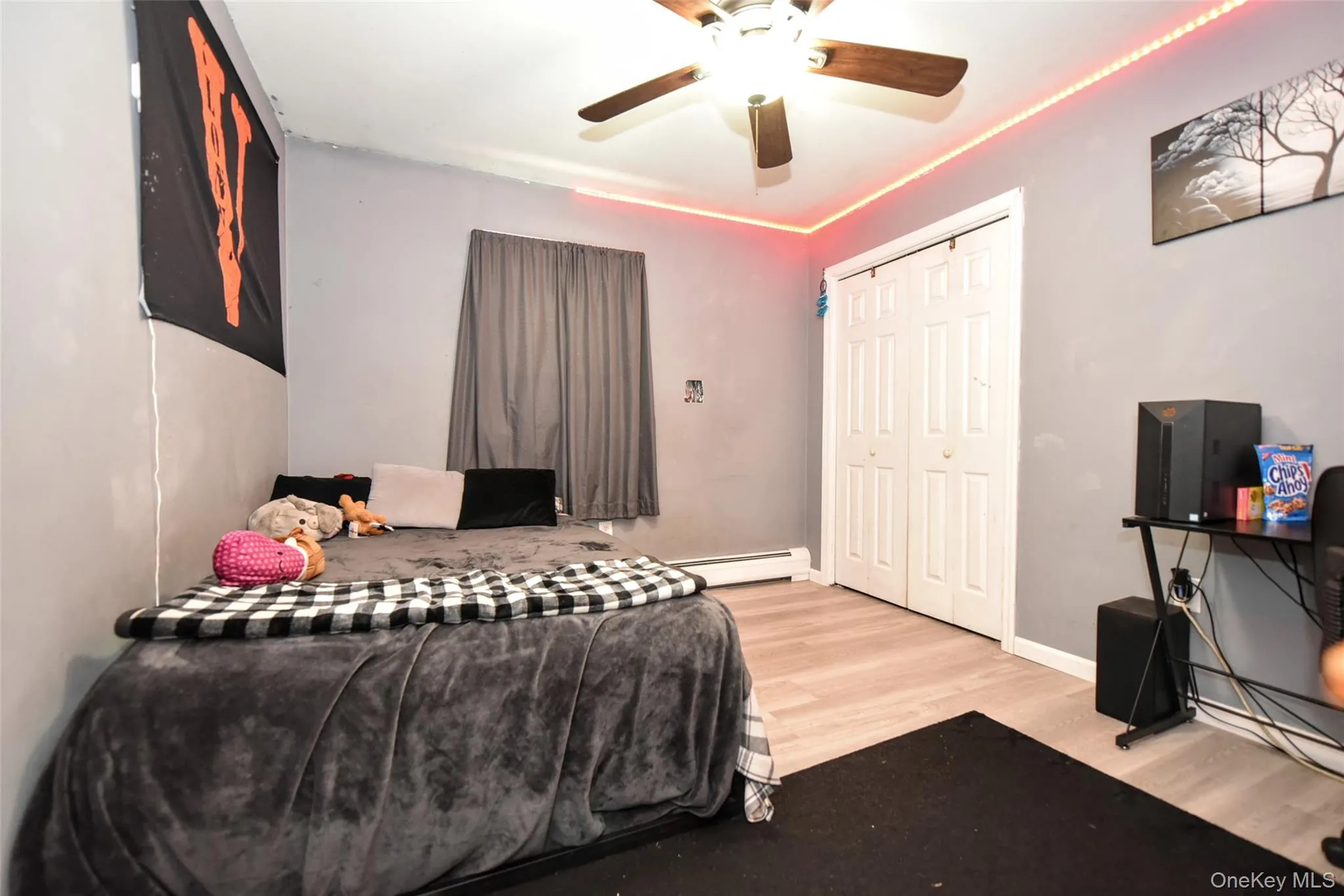Bedroom with light wood-style floors, a ceiling fan, a closet, and a baseboard heating unit Bedroom with light wood-style floors, a ceiling fan, a closet, and a baseboard heating unit