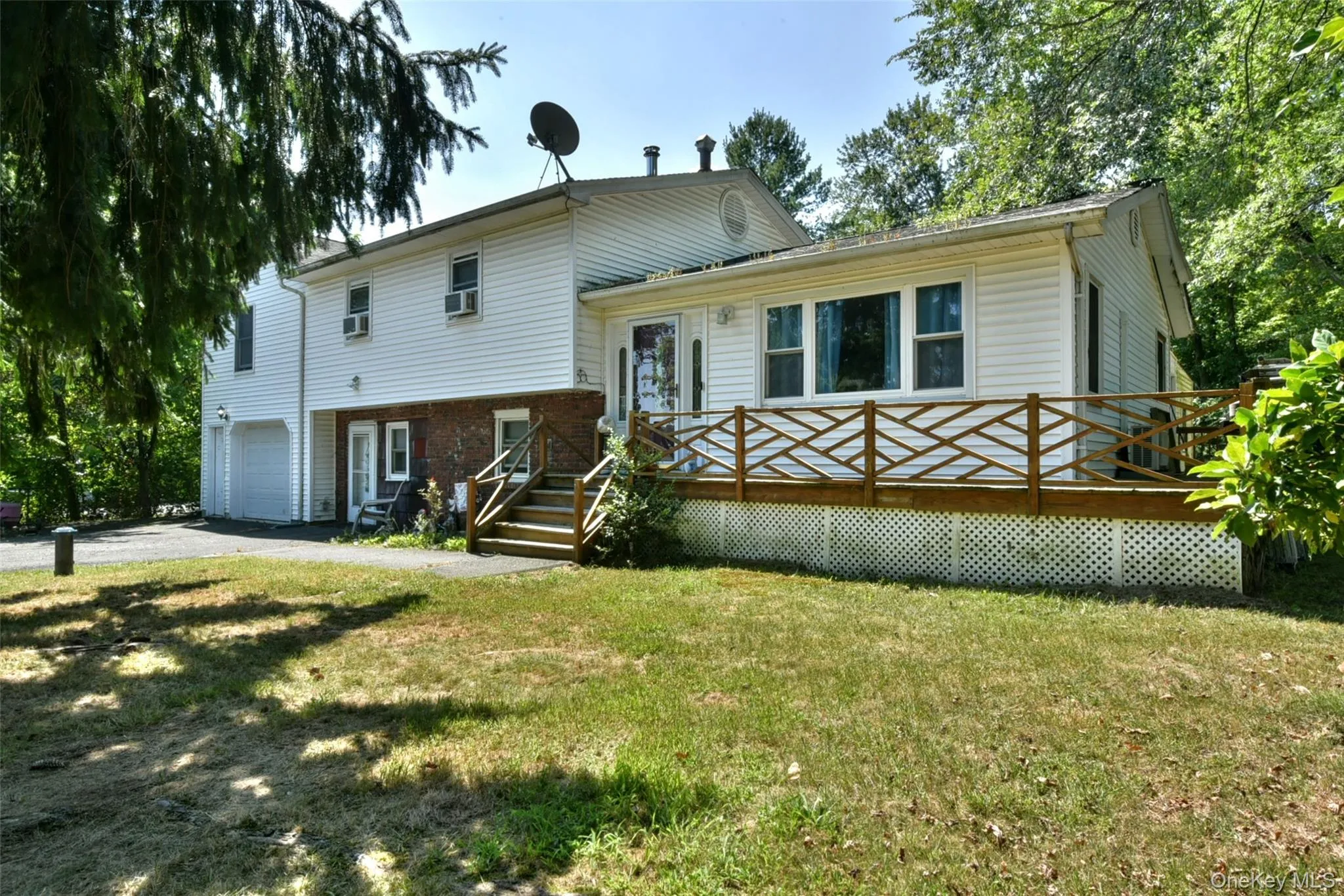 Split level home with a garage, a front yard, a wooden deck, and driveway Split level home with a garage, a front yard, a wooden deck, and driveway