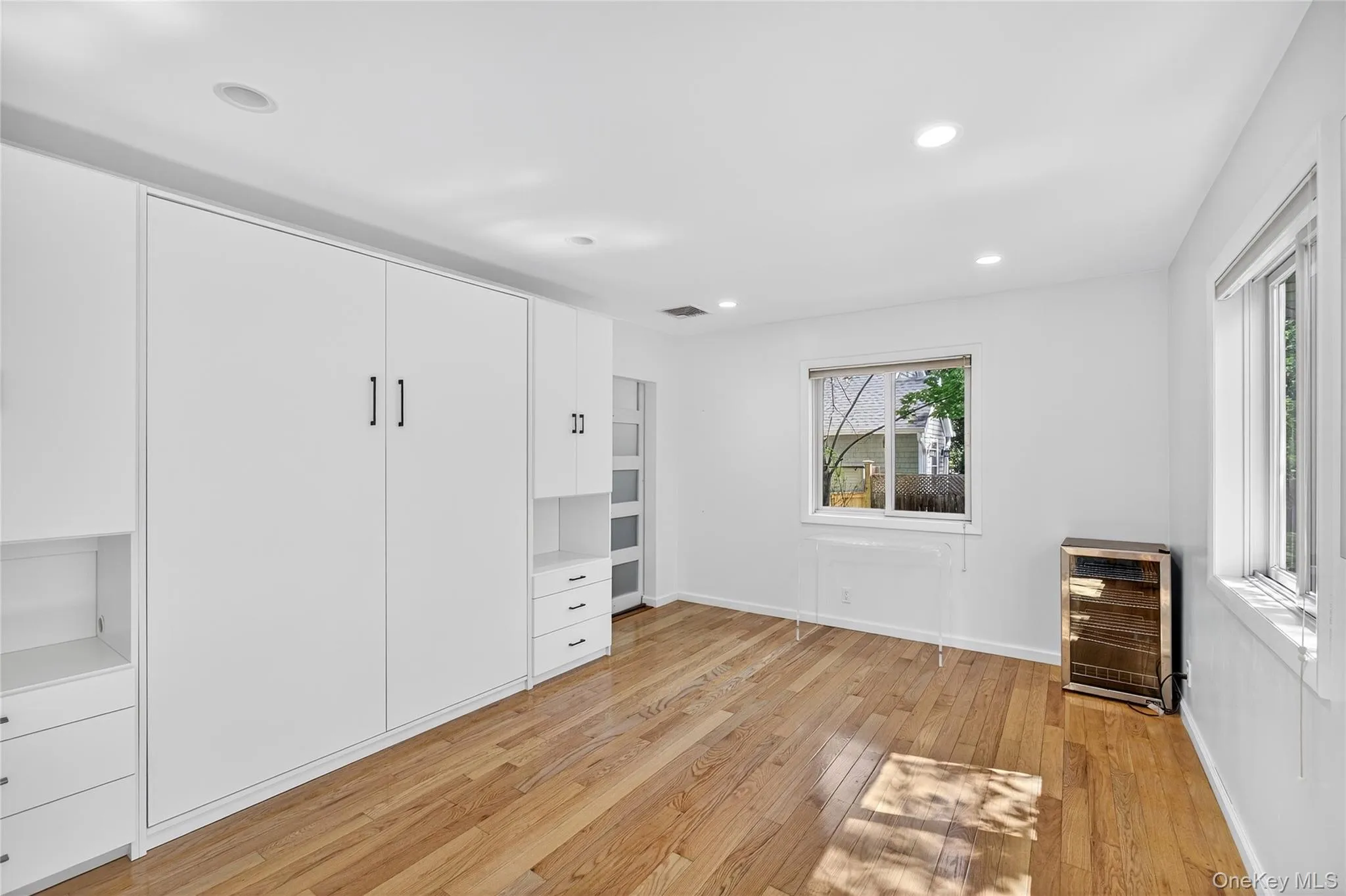 Primary Bedroom with Murphy bed or can be closed and used as a wall, stackable washer and clothes dryer in separate laundry room as seen light wood-type flooring, and recessed lighting Primary Bedroom with Murphy bed or can be closed and used as a wall, stackable washer and clothes dryer in separate laundry room as seen light wood-type flooring, and recessed lighting