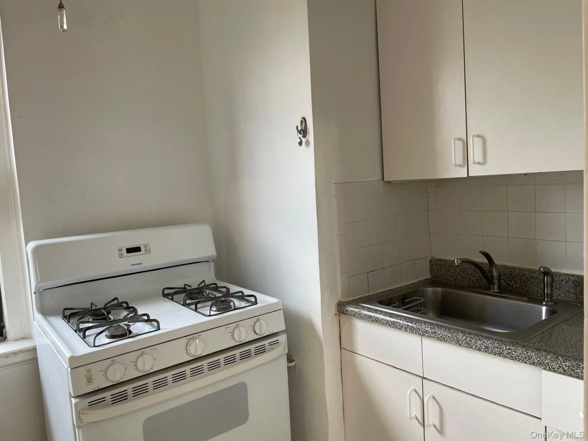 Kitchen with white gas range, white cabinetry, dark countertops, and tasteful backsplash Kitchen with white gas range, white cabinetry, dark countertops, and tasteful backsplash