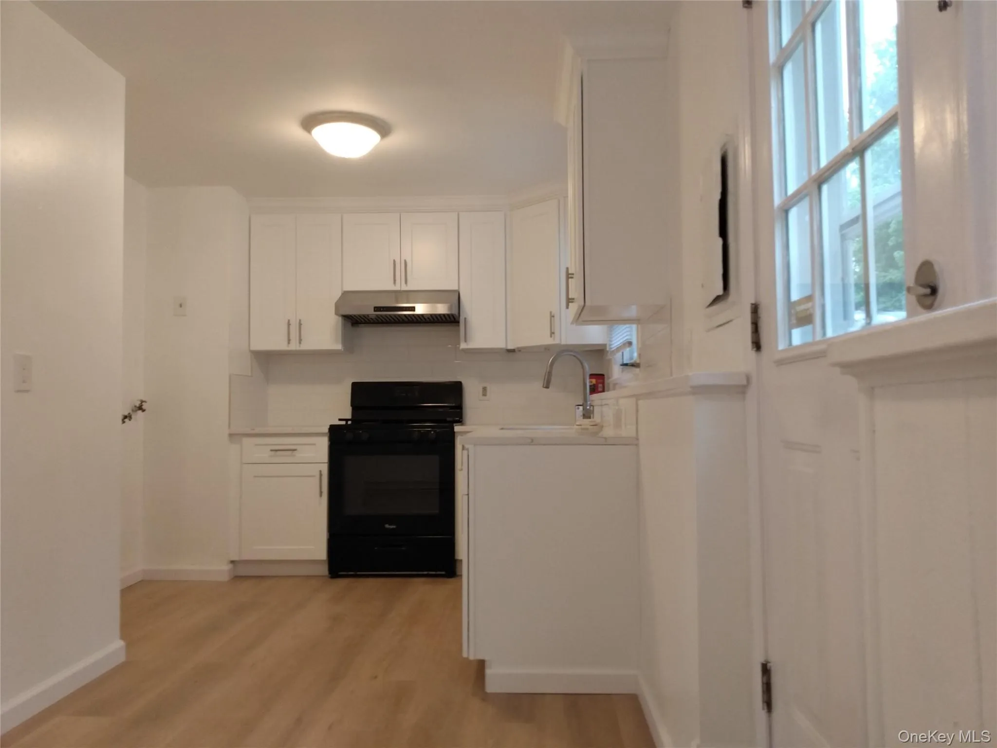 Kitchen featuring white cabinets, black range with gas stovetop, light countertops, tasteful backsplash, and light color flooring Kitchen featuring white cabinets, black range with gas stovetop, light countertops, tasteful backsplash, and light color flooring