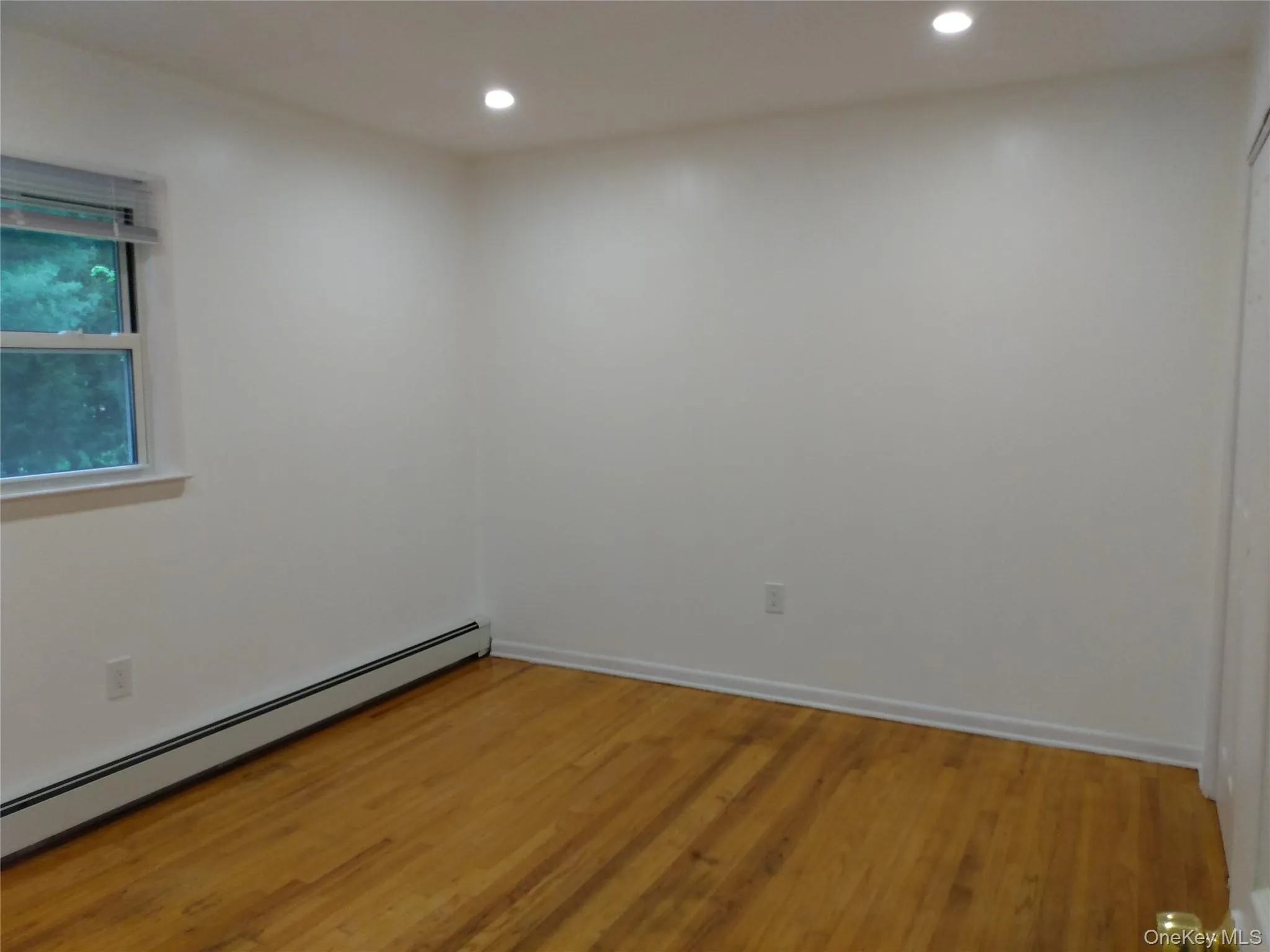 Unfurnished room with hardwood floors, a baseboard heating unit, and recessed lighting Unfurnished room with hardwood floors, a baseboard heating unit, and recessed lighting