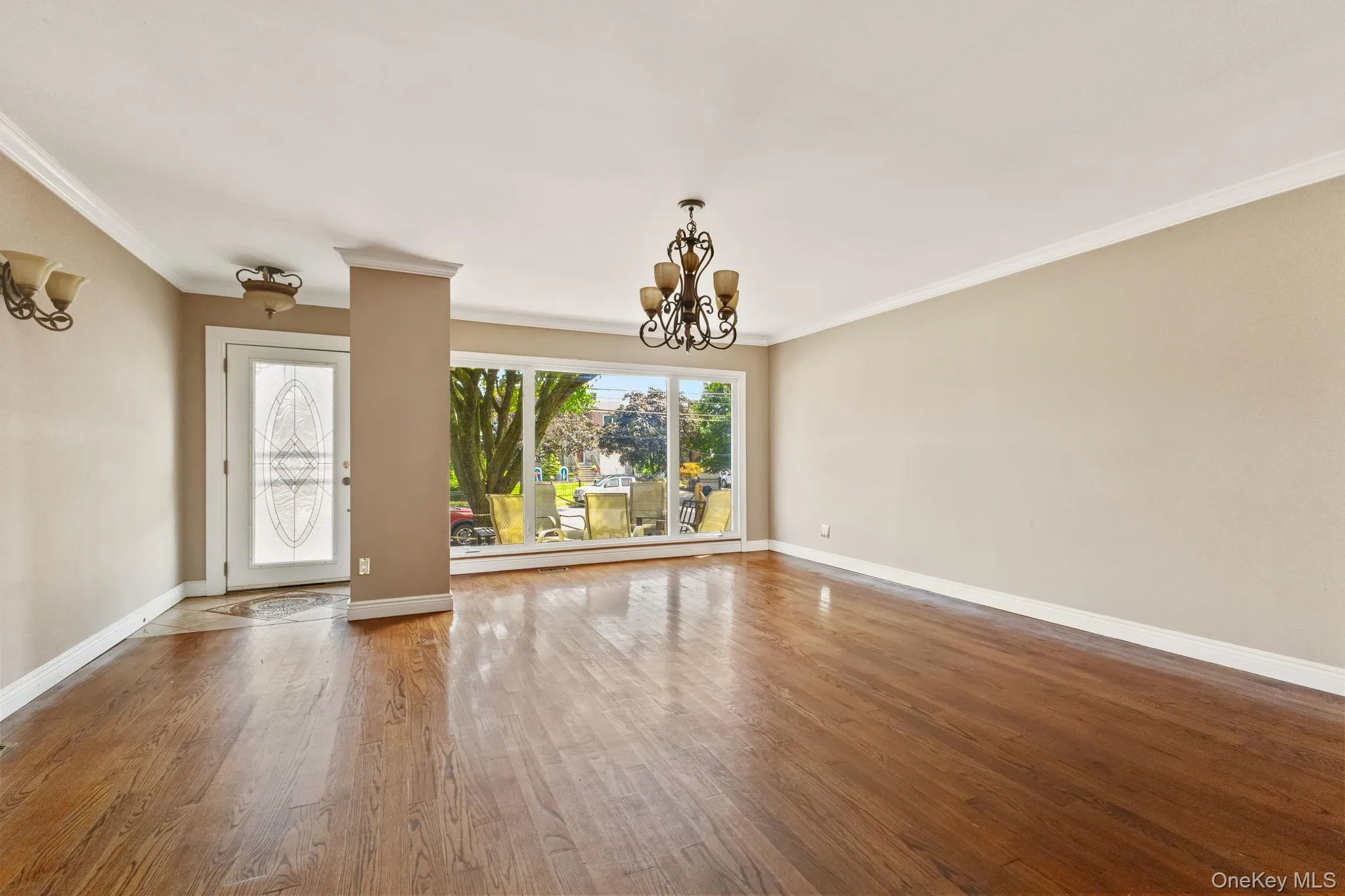 Unfurnished living room featuring a chandelier, ornamental molding, and wood finished floors Unfurnished living room featuring a chandelier, ornamental molding, and wood finished floors