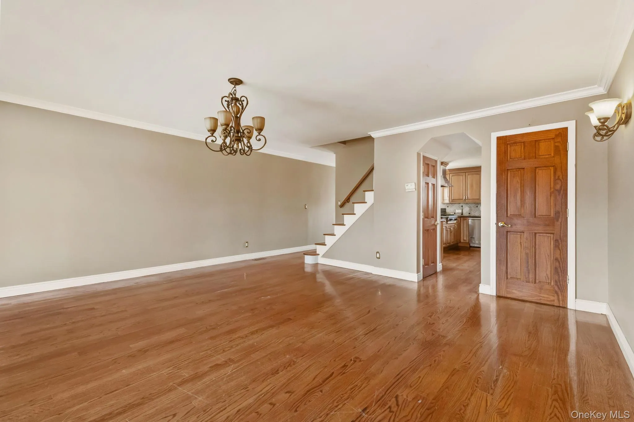 Unfurnished room featuring crown molding, stairway, light wood-style flooring, arched walkways, and a chandelier Unfurnished room featuring crown molding, stairway, light wood-style flooring, arched walkways, and a chandelier