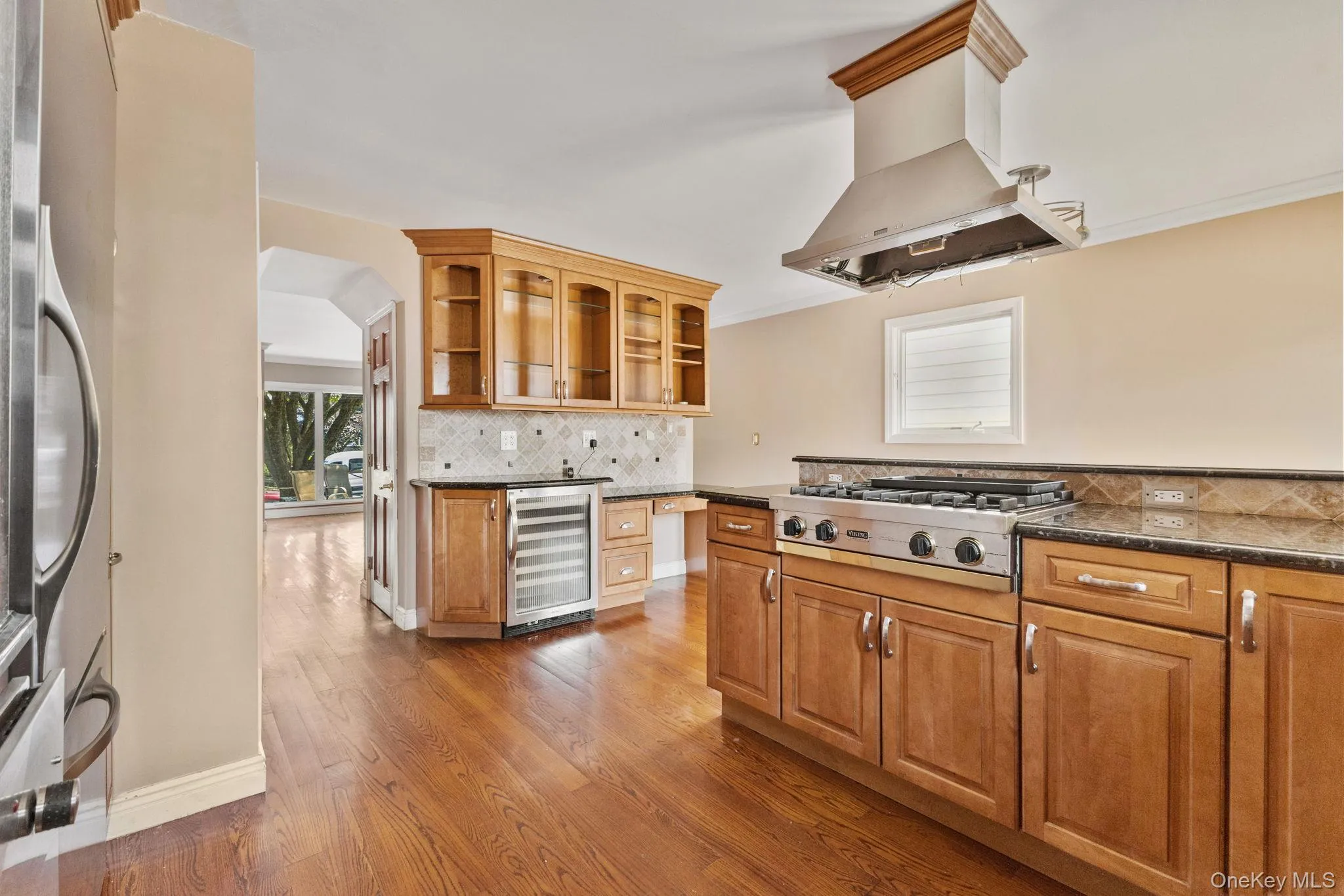 Kitchen with brown cabinets, island range hood, tasteful backsplash, wine cooler, and crown molding Kitchen with brown cabinets, island range hood, tasteful backsplash, wine cooler, and crown molding