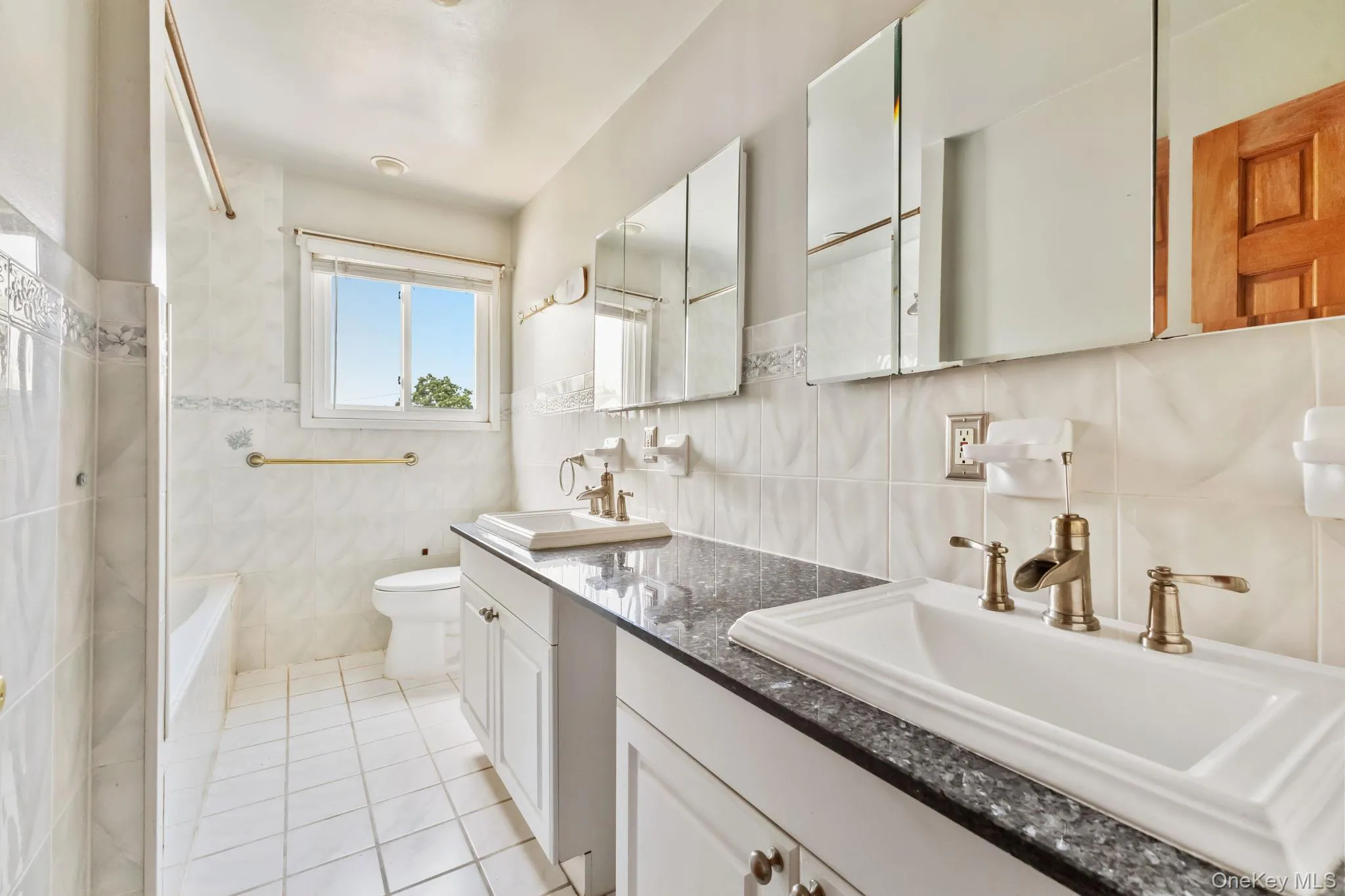 Full bathroom with tile walls, double vanity, light tile patterned flooring, shower / bathtub combination, and tasteful backsplash Full bathroom with tile walls, double vanity, light tile patterned flooring, shower / bathtub combination, and tasteful backsplash