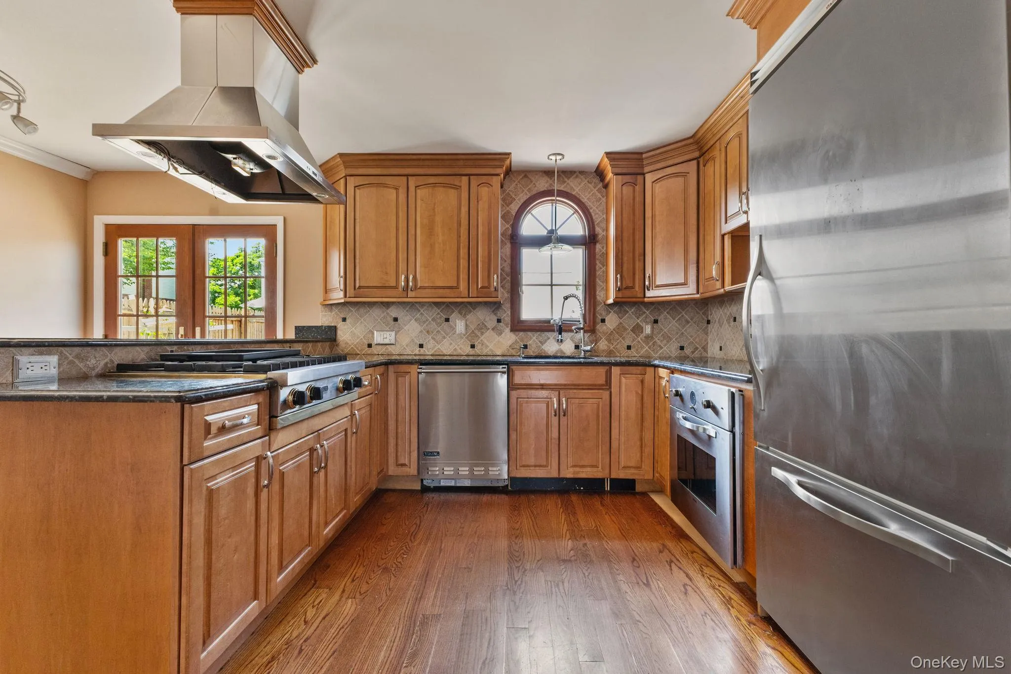 Kitchen with appliances with stainless steel finishes, brown cabinets, island range hood, dark stone counters, and crown molding Kitchen with appliances with stainless steel finishes, brown cabinets, island range hood, dark stone counters, and crown molding