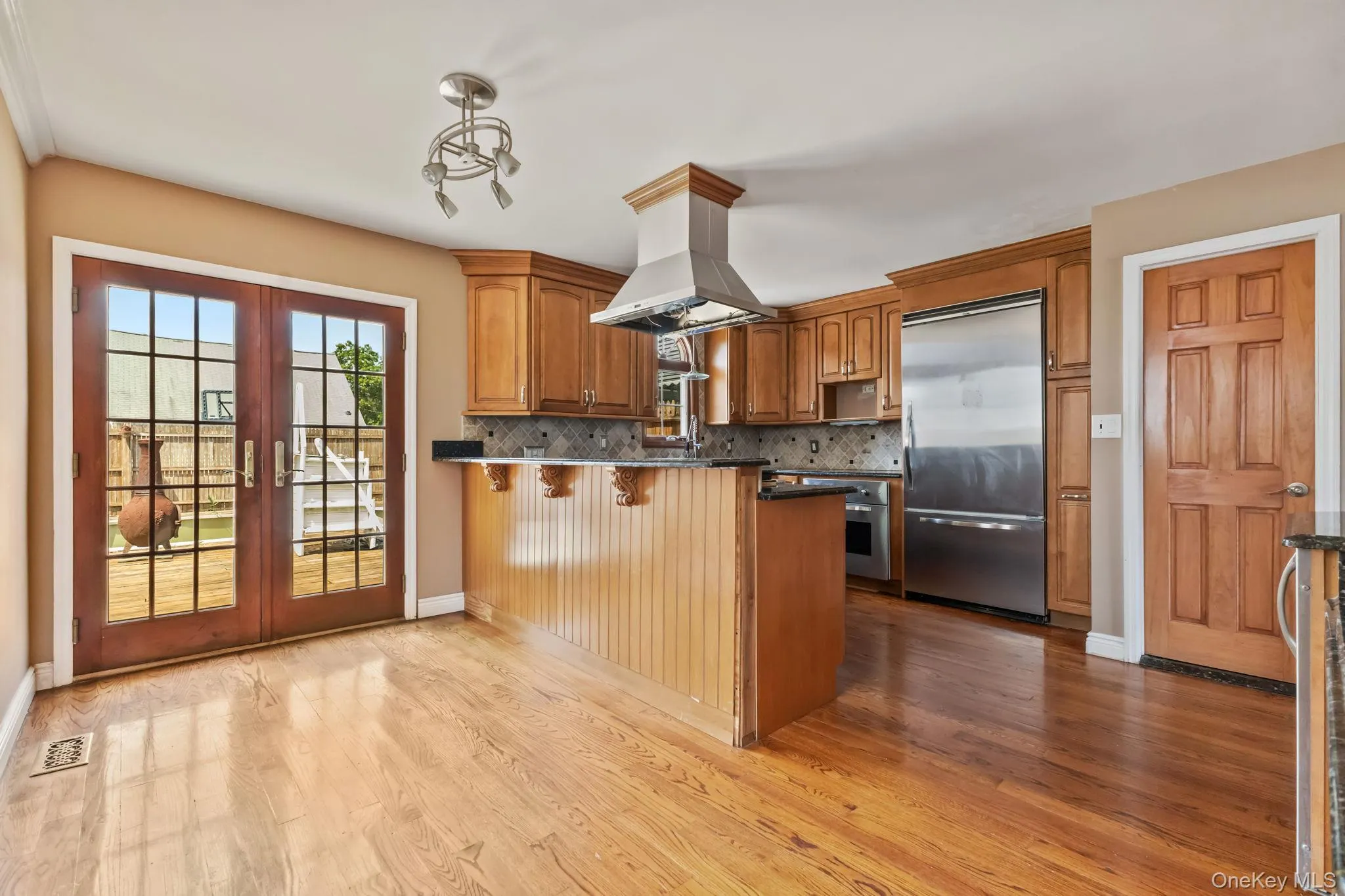 Kitchen featuring a kitchen breakfast bar, stainless steel built in refrigerator, brown cabinets, a peninsula, and tasteful backsplash Kitchen featuring a kitchen breakfast bar, stainless steel built in refrigerator, brown cabinets, a peninsula, and tasteful backsplash