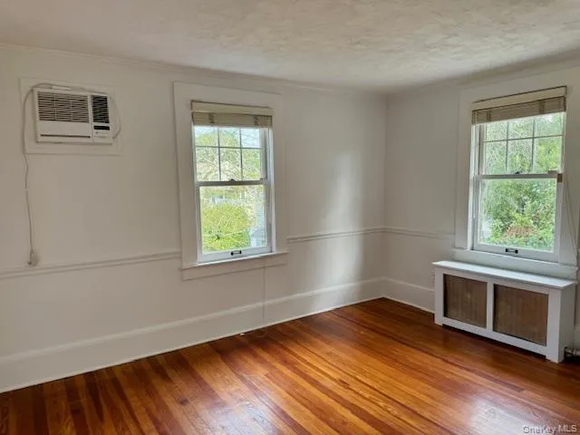 Bedroom featuring radiator, hardwood / wood-style flooring, a wall unit AC, a textured ceiling, and ornamental molding Bedroom featuring radiator, hardwood / wood-style flooring, a wall unit AC, a textured ceiling, and ornamental molding