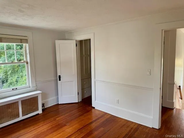 Unfurnished bedroom featuring radiator, dark wood-style flooring, ornamental molding, and a textured ceiling Unfurnished bedroom featuring radiator, dark wood-style flooring, ornamental molding, and a textured ceiling