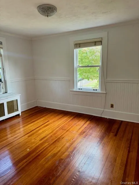 Unfurnished room featuring light wood-style flooring, crown molding, radiator heating unit, wainscoting, and a textured ceiling Unfurnished room featuring light wood-style flooring, crown molding, radiator heating unit, wainscoting, and a textured ceiling