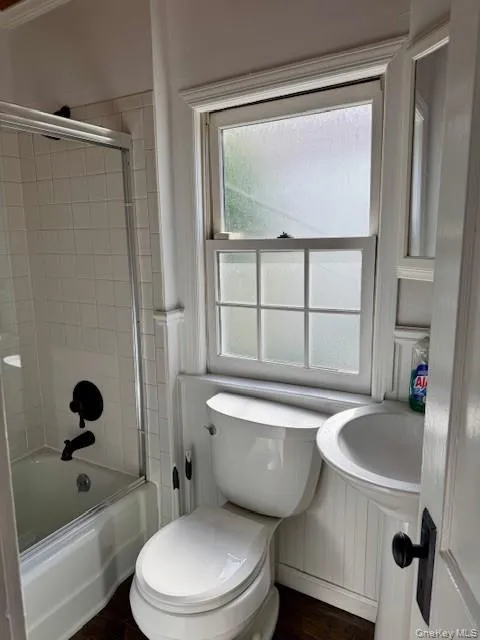 Full bath with combined bath / shower with glass door and dark wood-style flooring Full bath with combined bath / shower with glass door and dark wood-style flooring