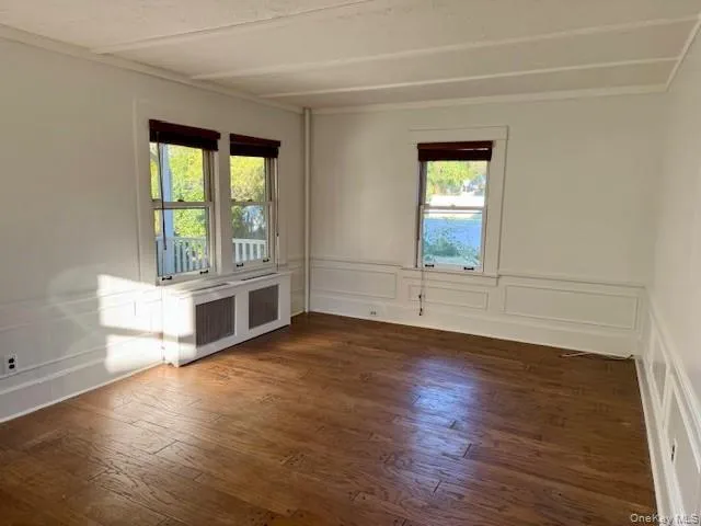 featuring a decorative wall, radiator, dark wood-style floors, and wainscoting featuring a decorative wall, radiator, dark wood-style floors, and wainscoting