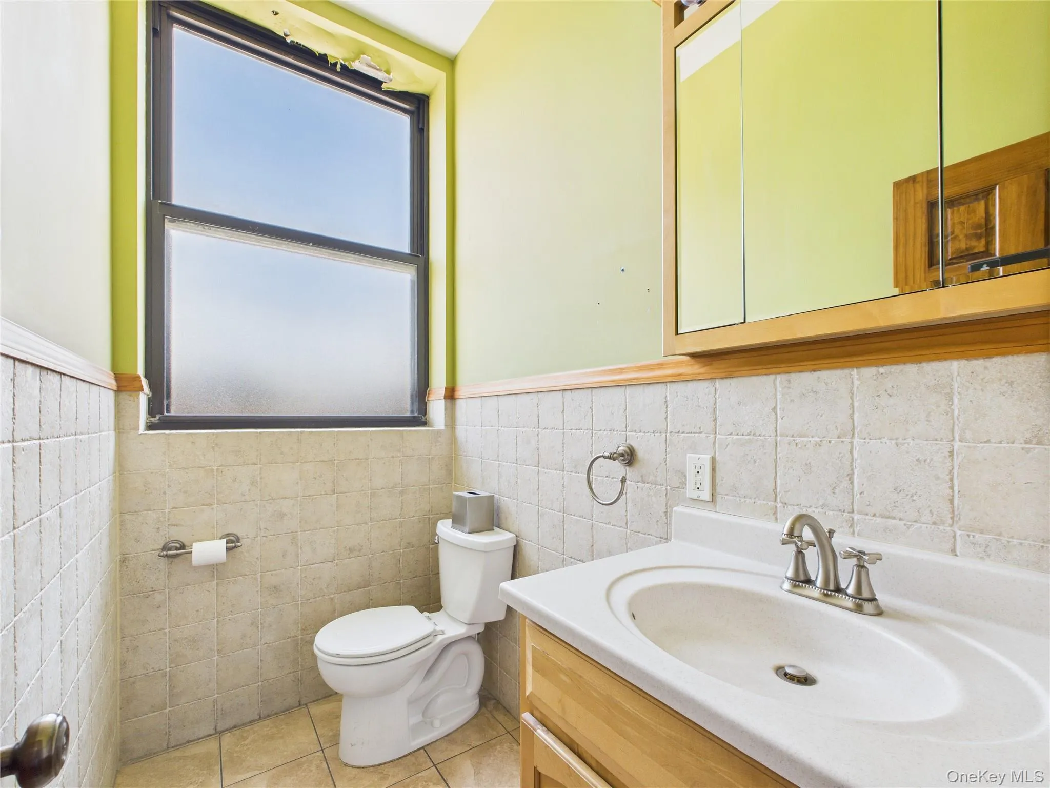 Half bath featuring vanity, light tile patterned flooring, a wainscoted wall, and tile walls Half bath featuring vanity, light tile patterned flooring, a wainscoted wall, and tile walls