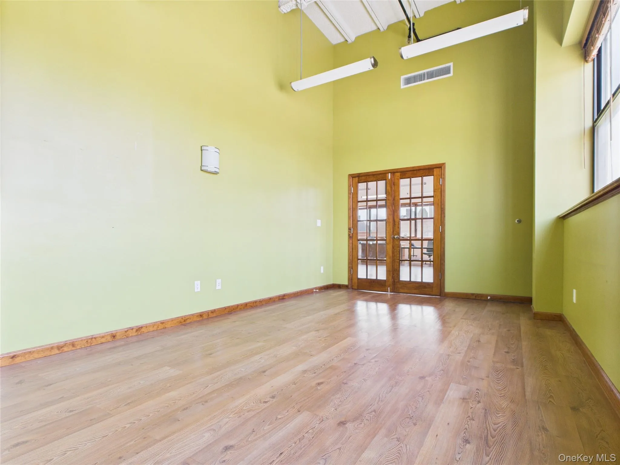 Empty room with healthy amount of natural light, wood finished floors, french doors, and a high ceiling Empty room with healthy amount of natural light, wood finished floors, french doors, and a high ceiling