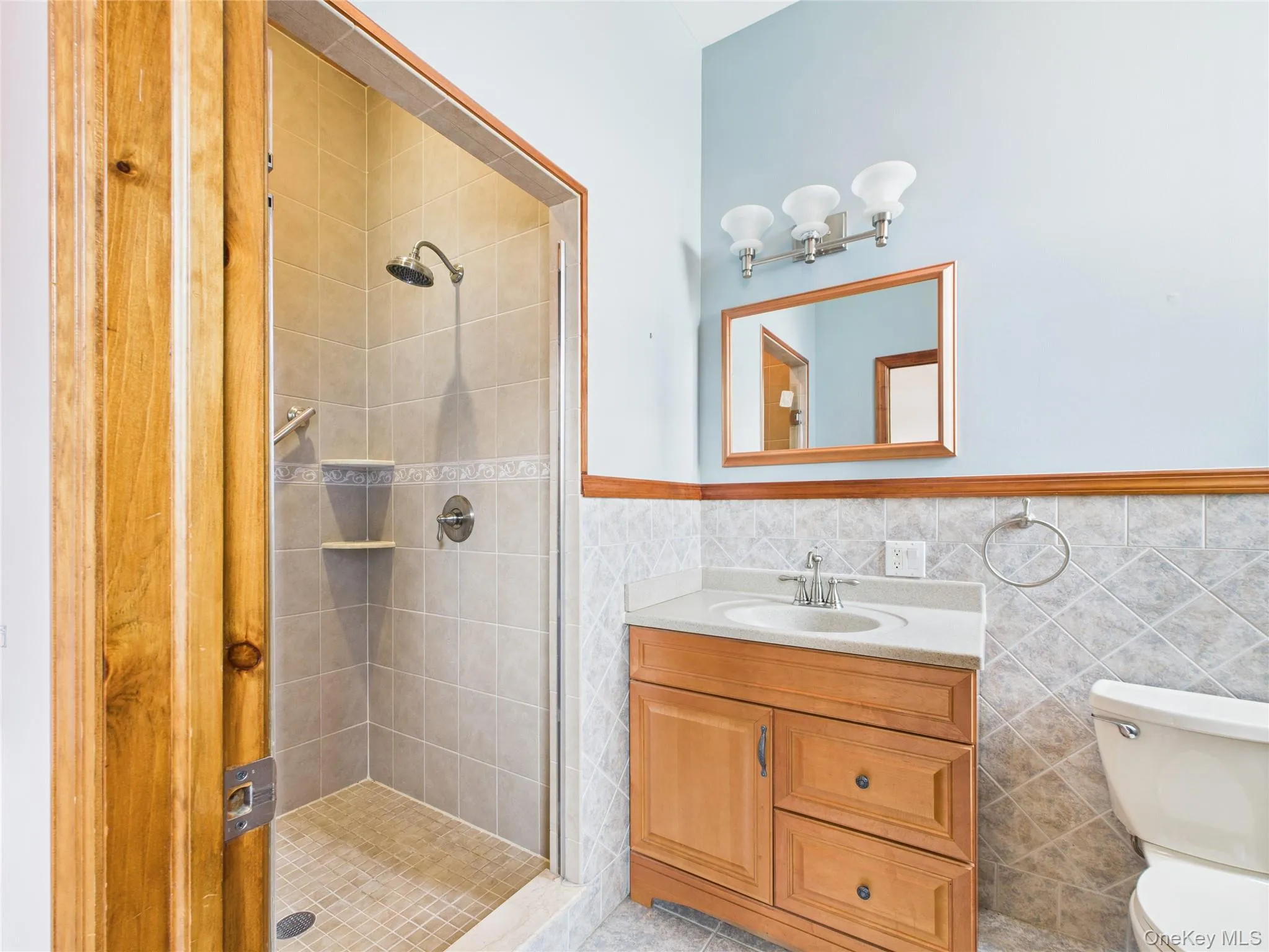 Bathroom featuring a stall shower, vanity, tile walls, and wainscoting Bathroom featuring a stall shower, vanity, tile walls, and wainscoting