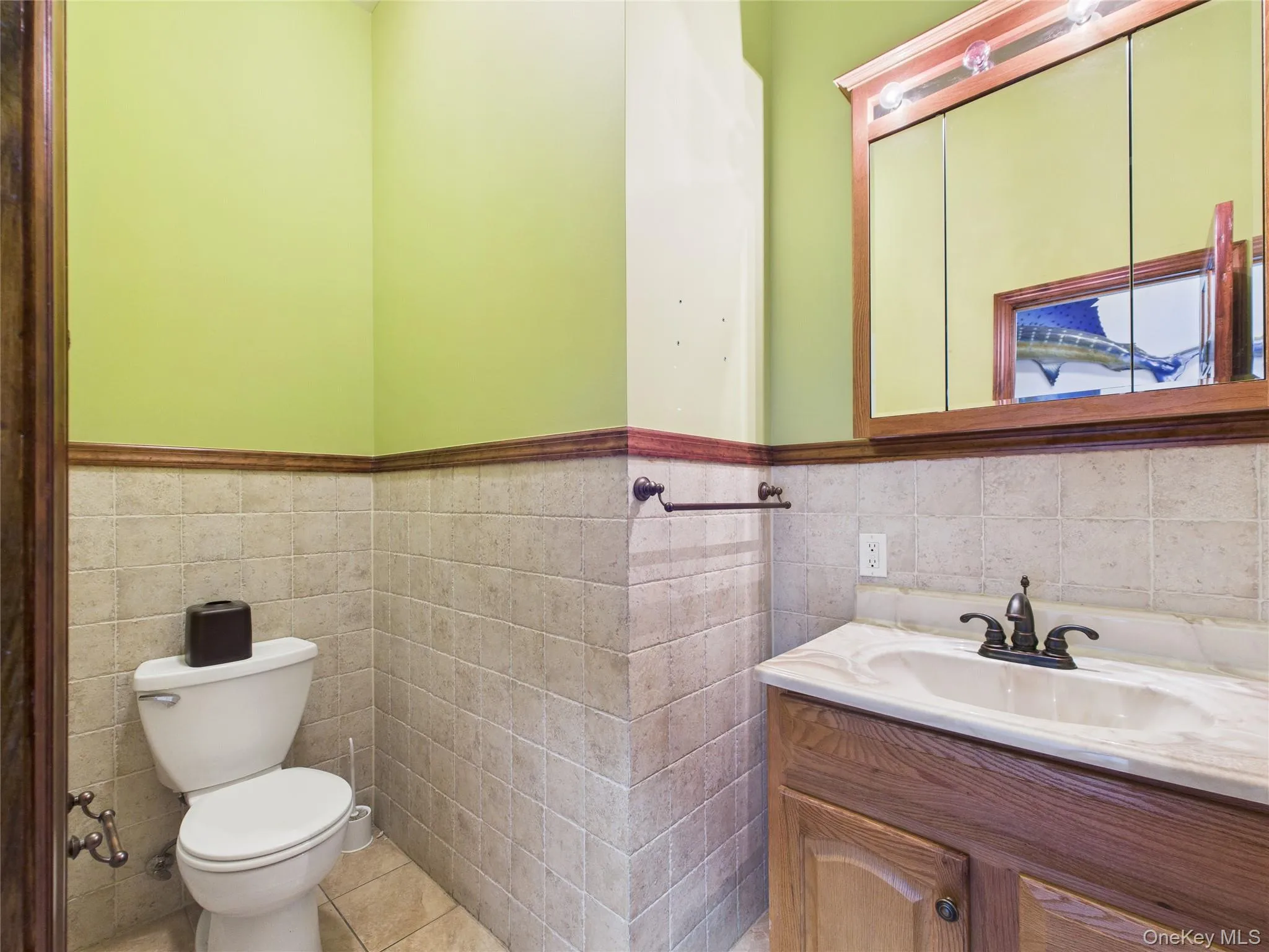 Bathroom featuring tile walls, vanity, wainscoting, and light tile patterned floors Bathroom featuring tile walls, vanity, wainscoting, and light tile patterned floors