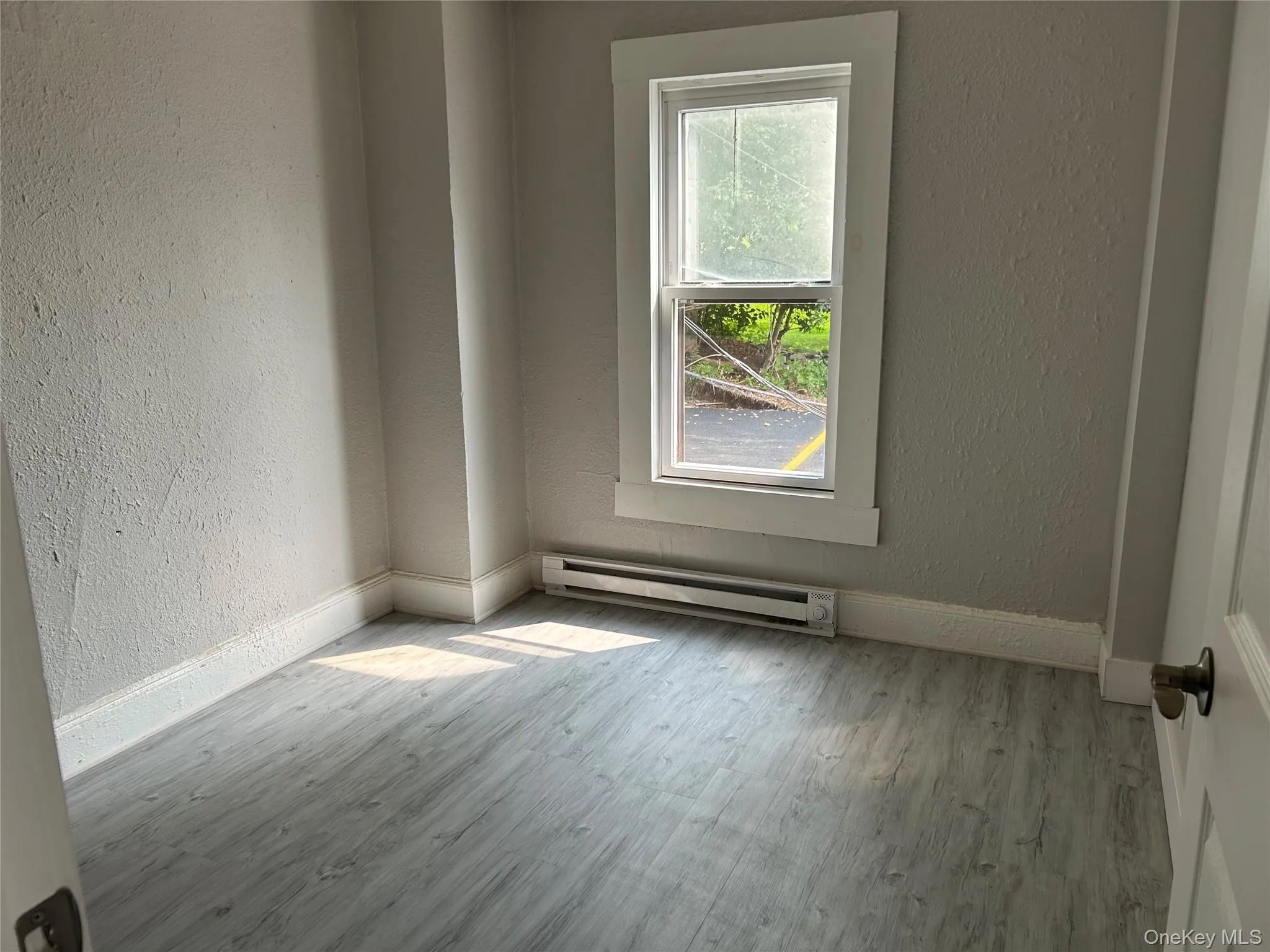 Unfurnished room with a textured wall, a baseboard heating unit, and wood finished floors Unfurnished room with a textured wall, a baseboard heating unit, and wood finished floors