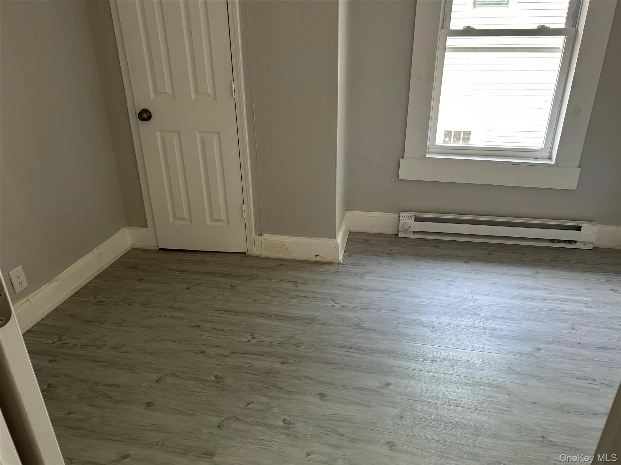 Unfurnished room with wood finished floors and baseboard heating Unfurnished room with wood finished floors and baseboard heating