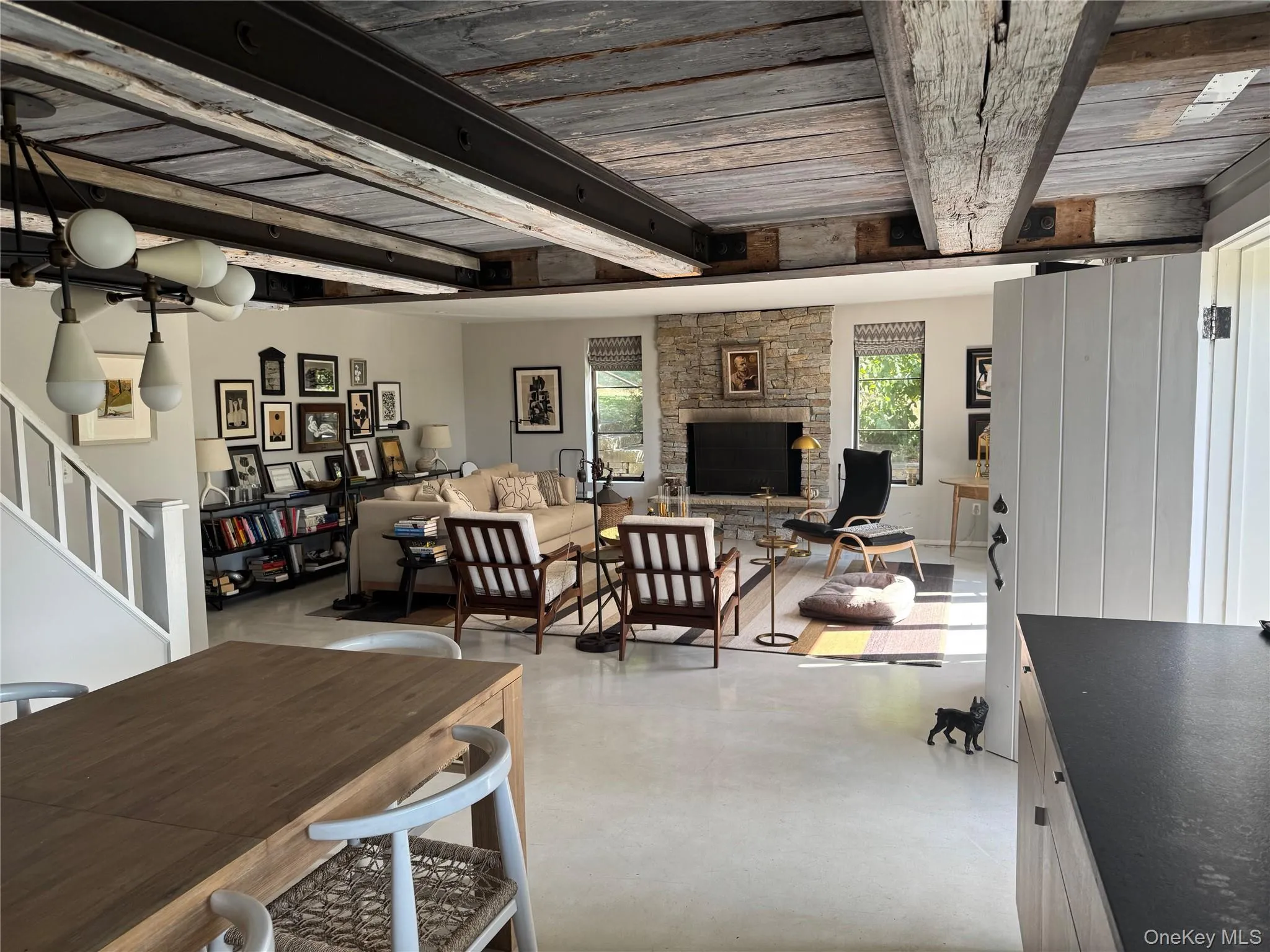 Dining space featuring stairs, a stone fireplace, finished concrete floors, and a wooden ceiling with exposed beams Dining space featuring stairs, a stone fireplace, finished concrete floors, and a wooden ceiling with exposed beams