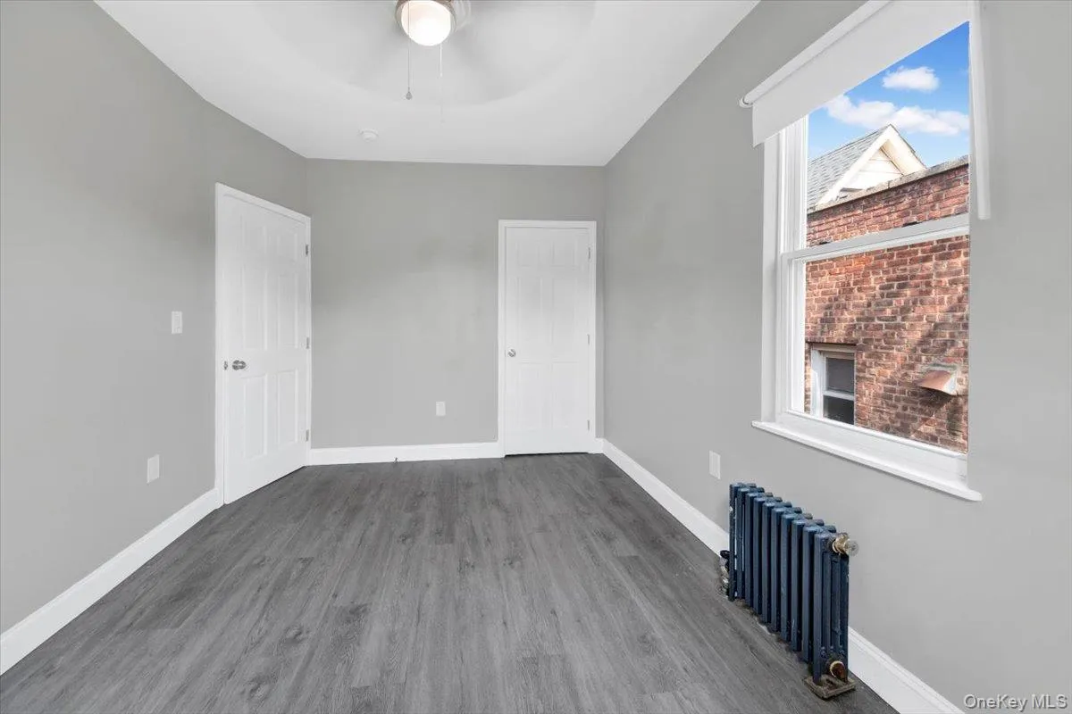 Unfurnished bedroom featuring radiator, wood finished floors, and ceiling fan Unfurnished bedroom featuring radiator, wood finished floors, and ceiling fan