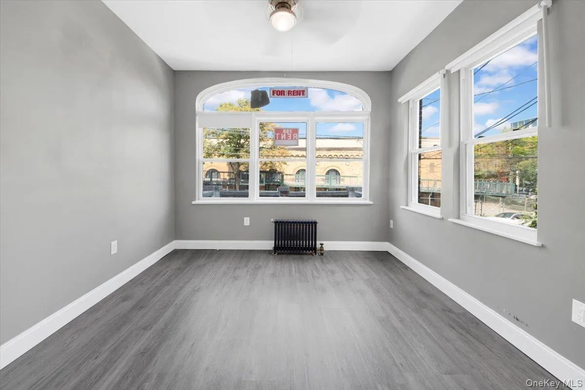 Unfurnished room with radiator, wood finished floors, and a ceiling fan Unfurnished room with radiator, wood finished floors, and a ceiling fan